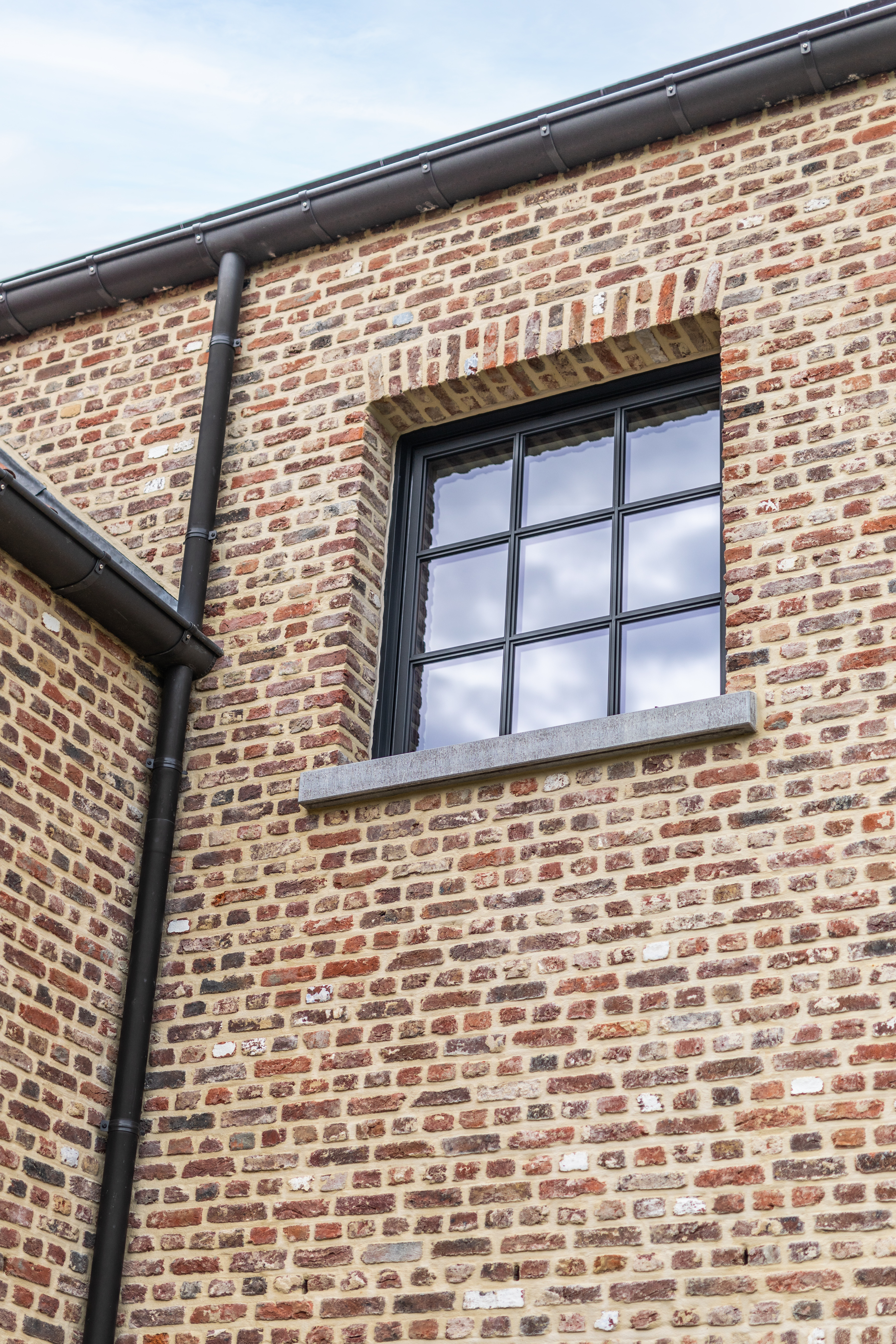 Zwart Steellook PLUS small draai-kipraam in een warme, landelijke bakstenen gevel van een nieuwbouwwoning.