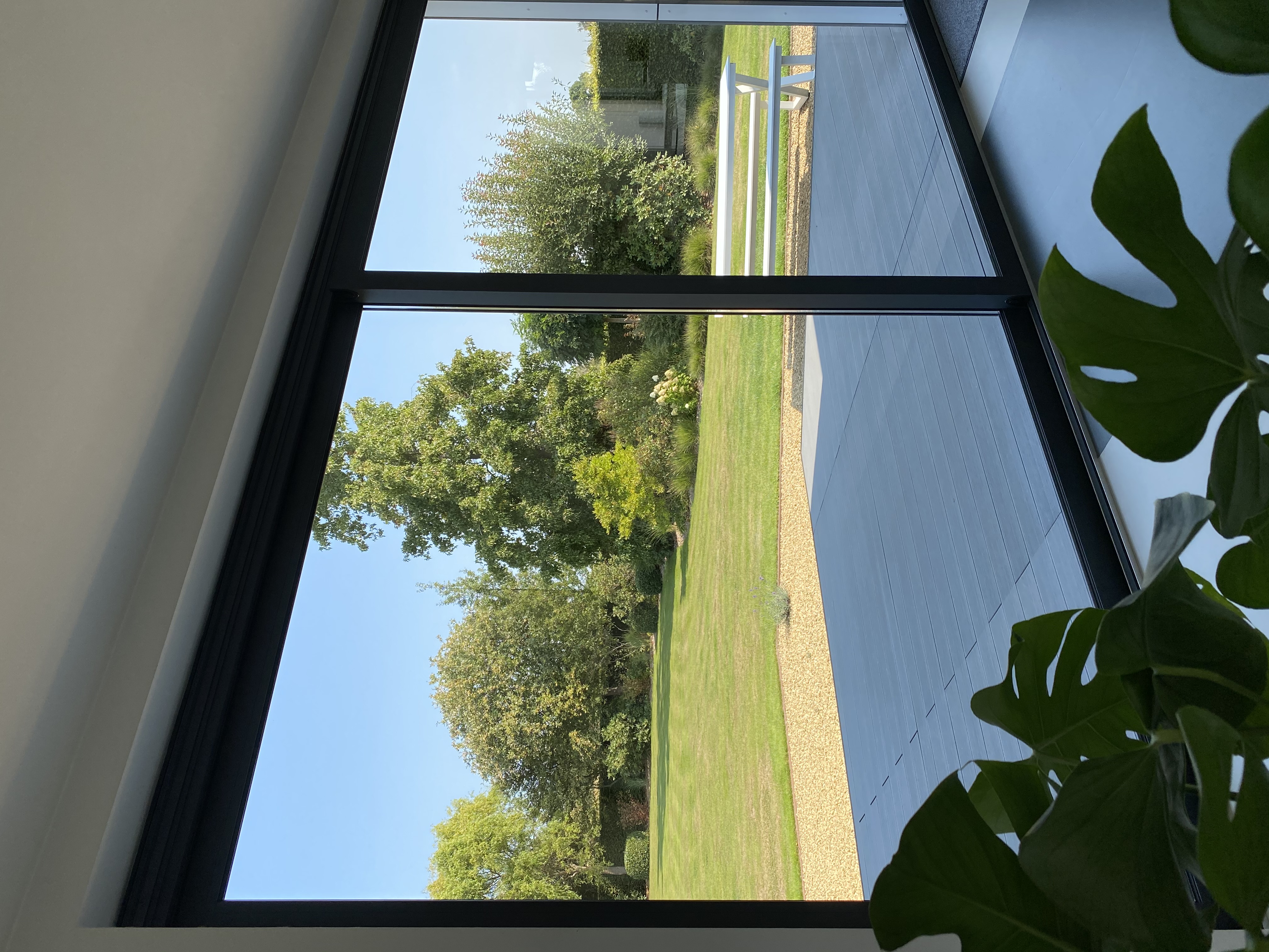 Zwart aluminium ALU Visoglide Duorail-schuifraam met grote glasvlakken kijkt vanuit een vrijstaande woning uit op een terras en een ruime groene tuin.