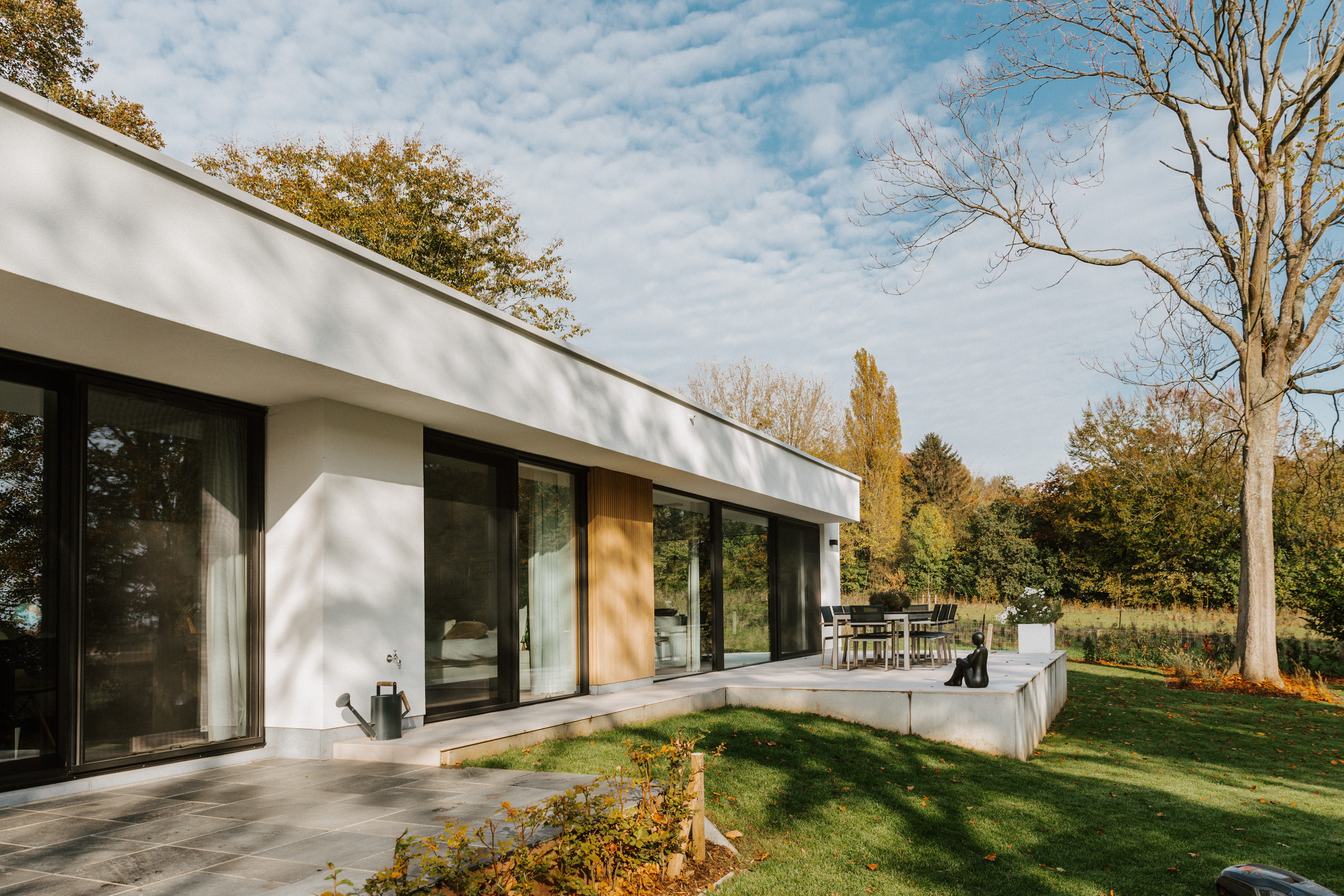 Moderne vrijstaande woning met zwarte aluminium schuiframen en een schuifvliegenraam, passend bij de gerenoveerde gevel en de groene tuin.