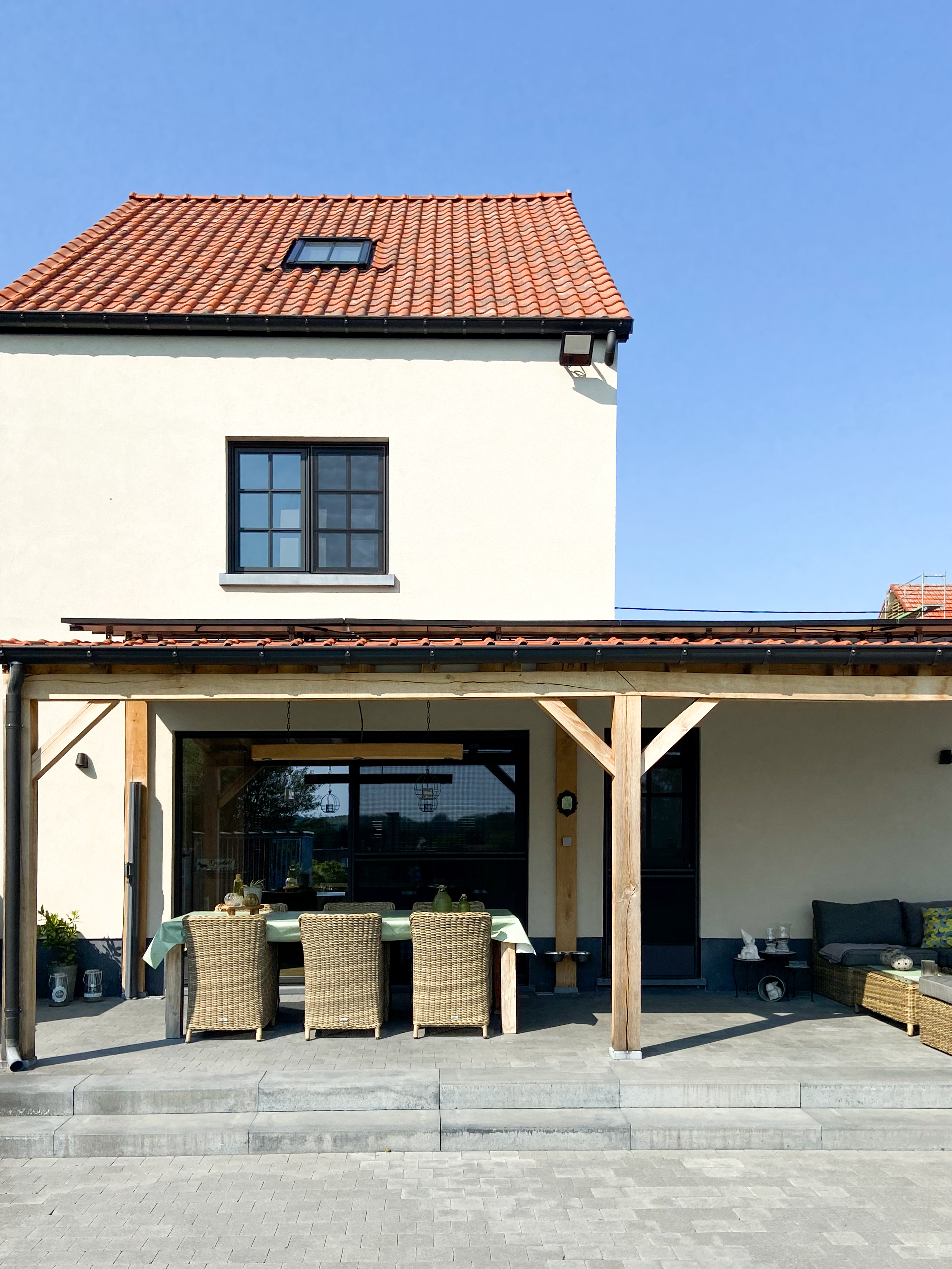 Gerenoveerde, witgepleisterde woning met rode dakpannen, zwarte Steellook PLUS small-raamprofielen, een dubbel raam en een draai-kipraam aan het overdekte terras.