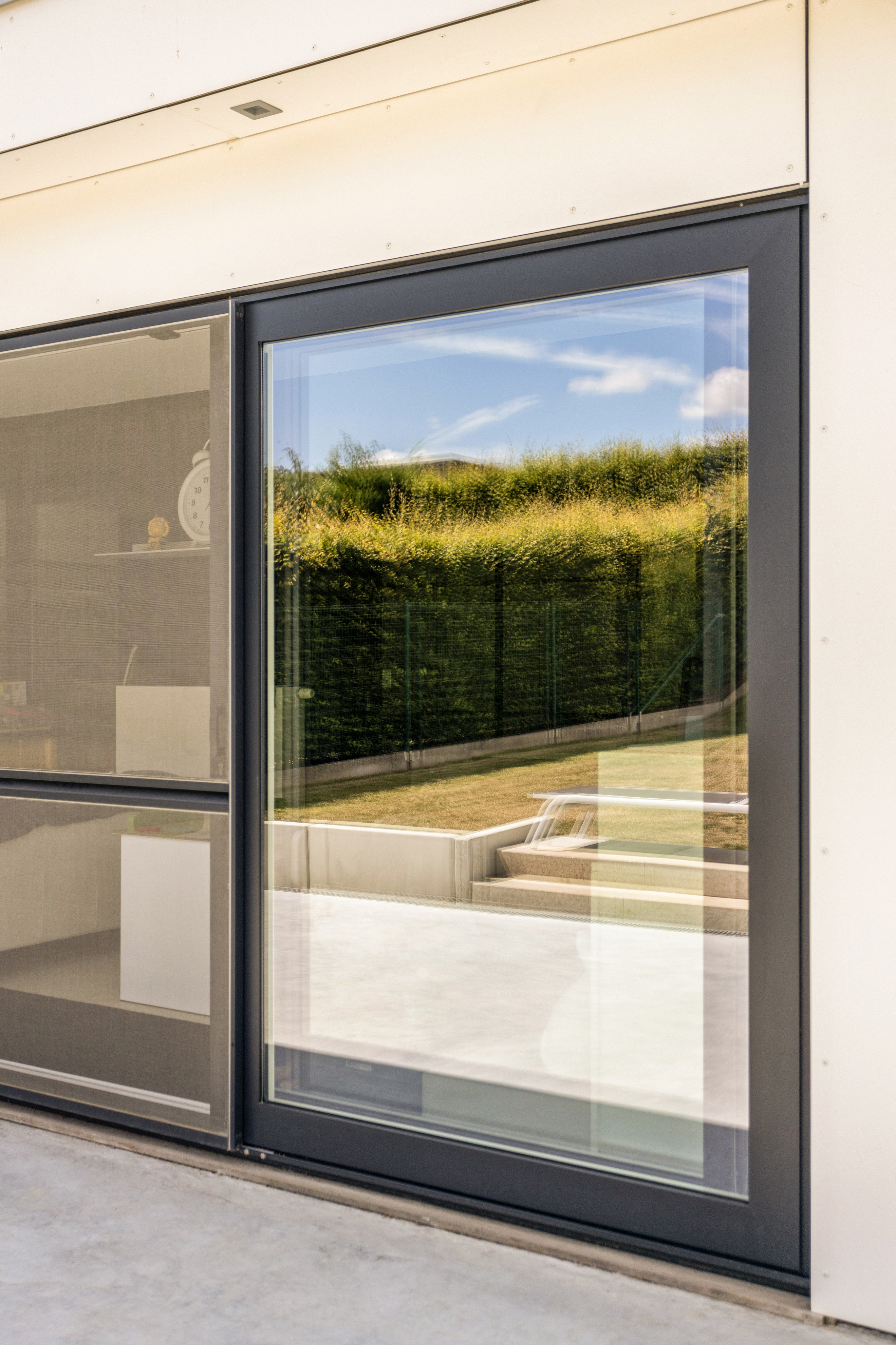 Diepzwart aluminium schuifvliegenraam in een Visoglide Duorail-systeem, met zicht op een groene tuin en een licht terras.