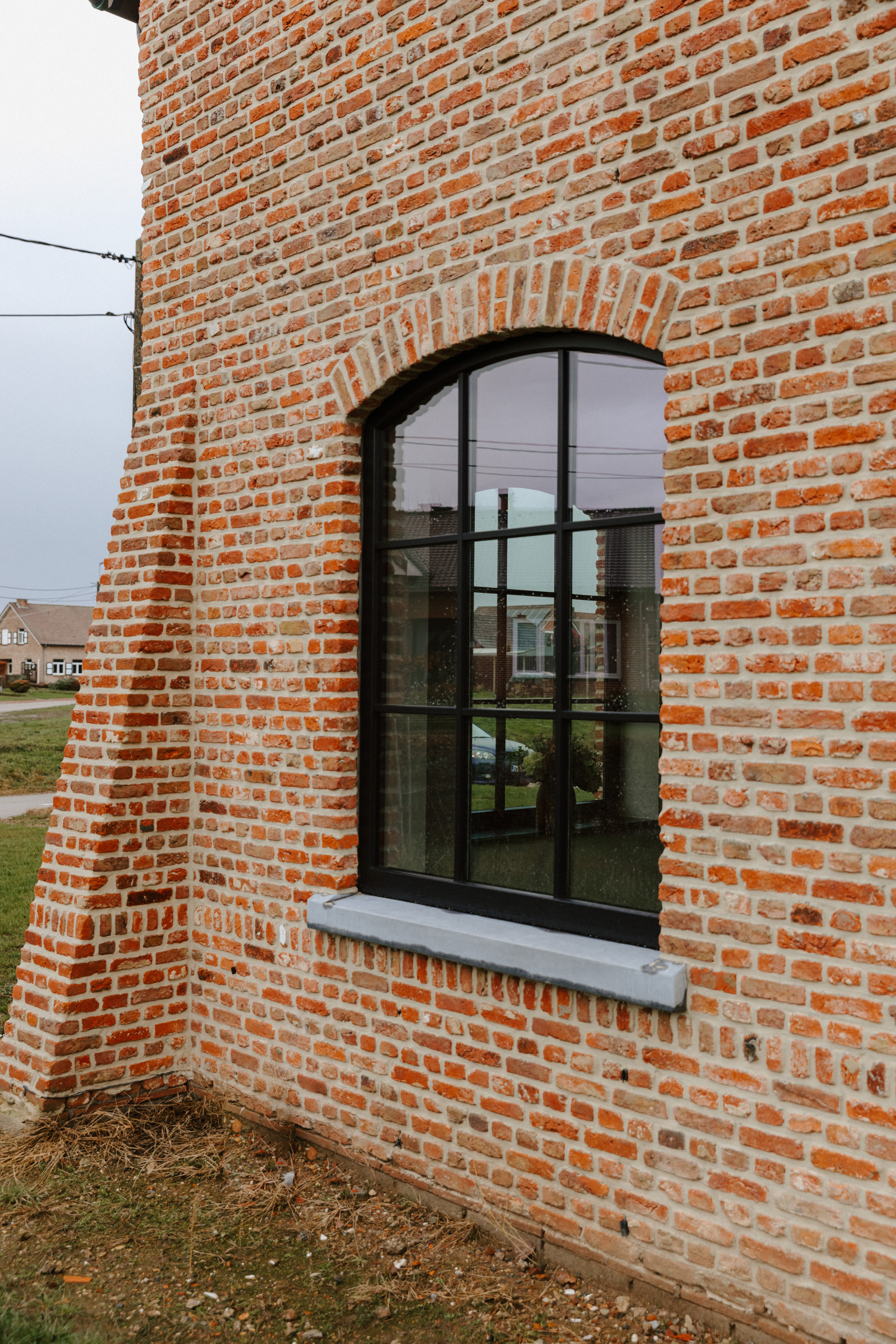 Vast Impakt PLUS-raam in matzwart, met een afgeronde boog, verwerkt in een warme, landelijke bakstenen gevel van een nieuwbouwwoning.