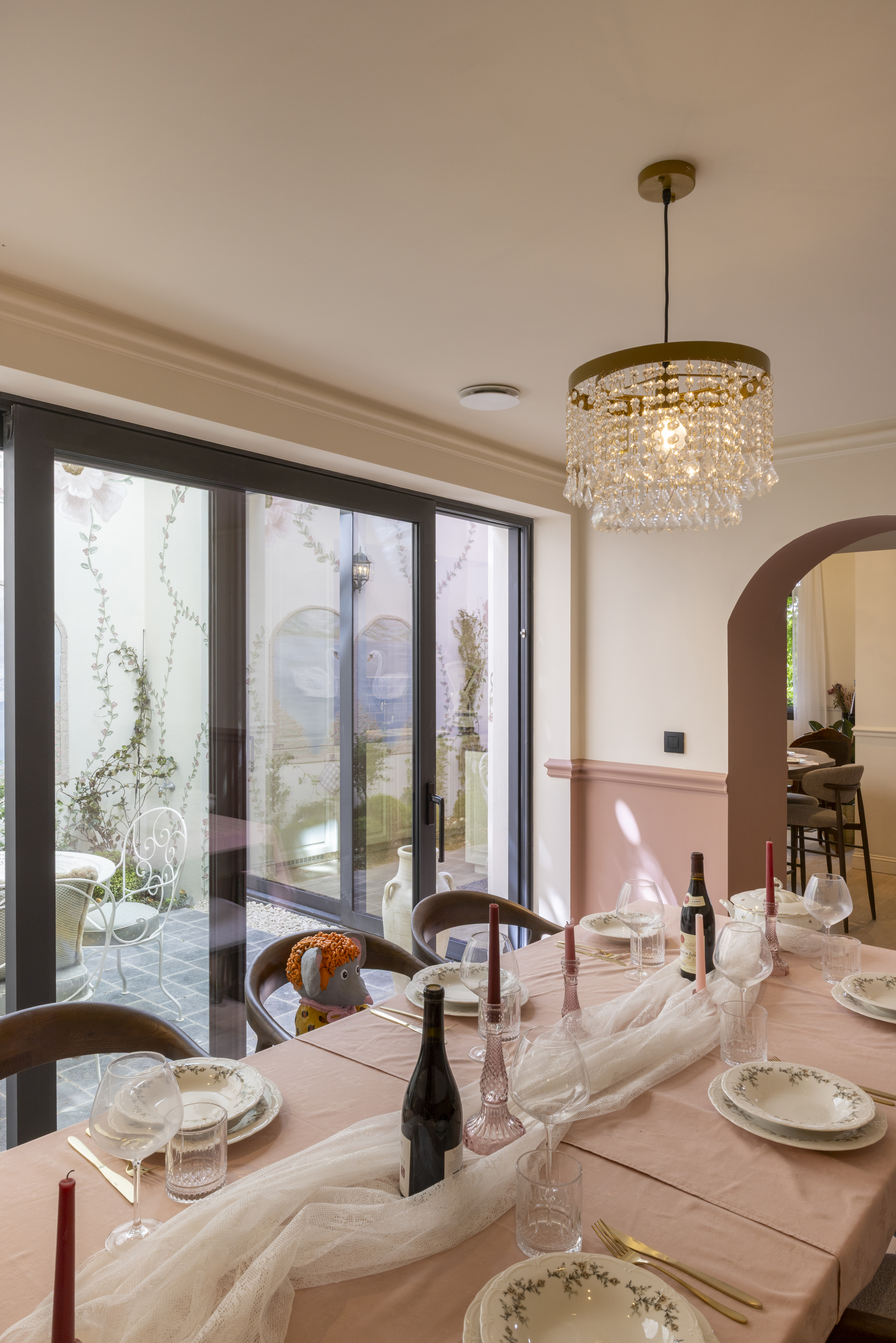 Groot aluminium schuifraam met mat bronzen profielen in een lichte eetkamer met stijlvol gedekte tafel en hanglamp.