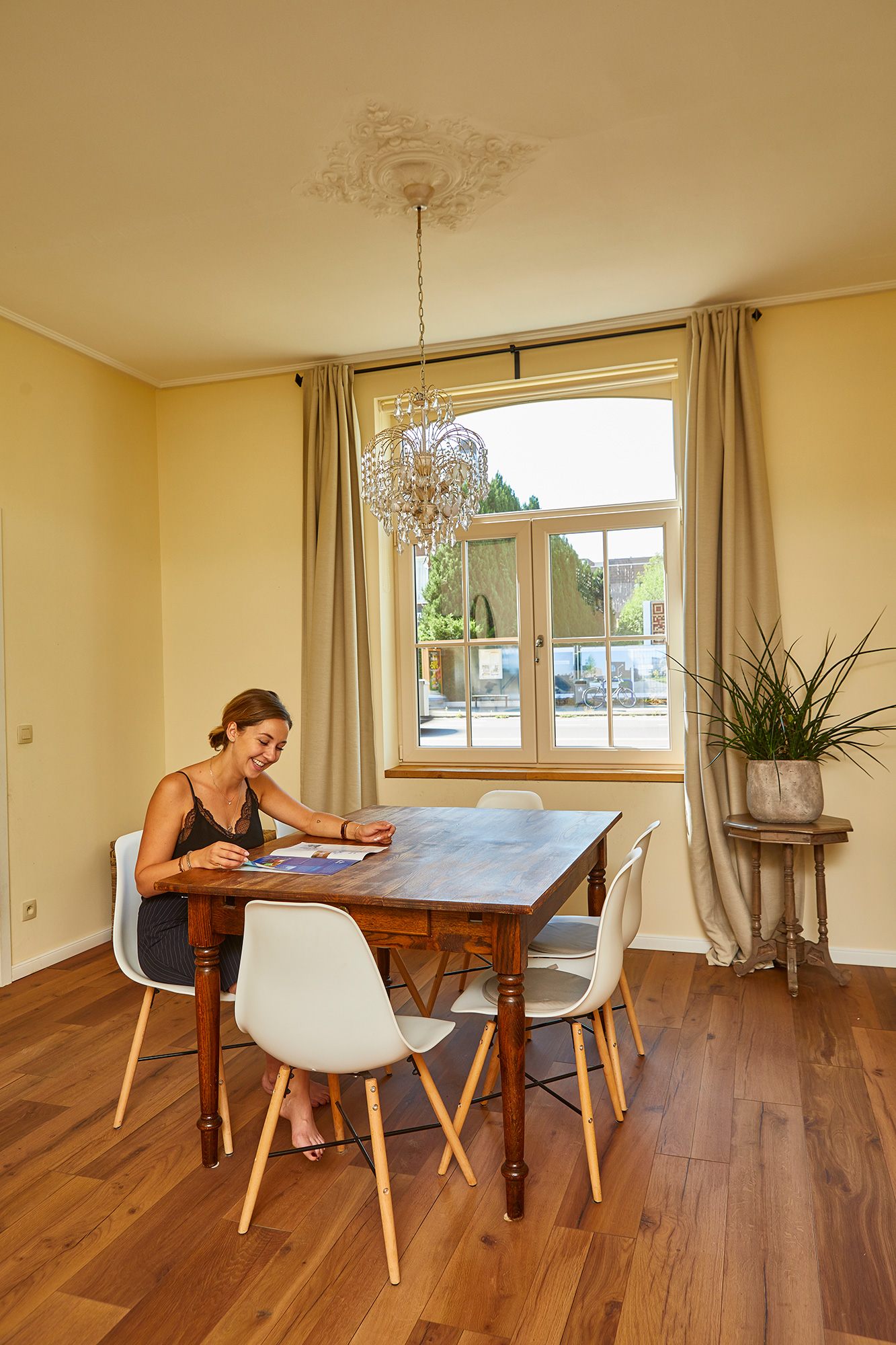 Lichte eetruimte in verfijnde klassieke stijl, met crèmekleurige muren, houten vloer, tafel en raam met elegante gordijnen in een gesloten bebouwing.