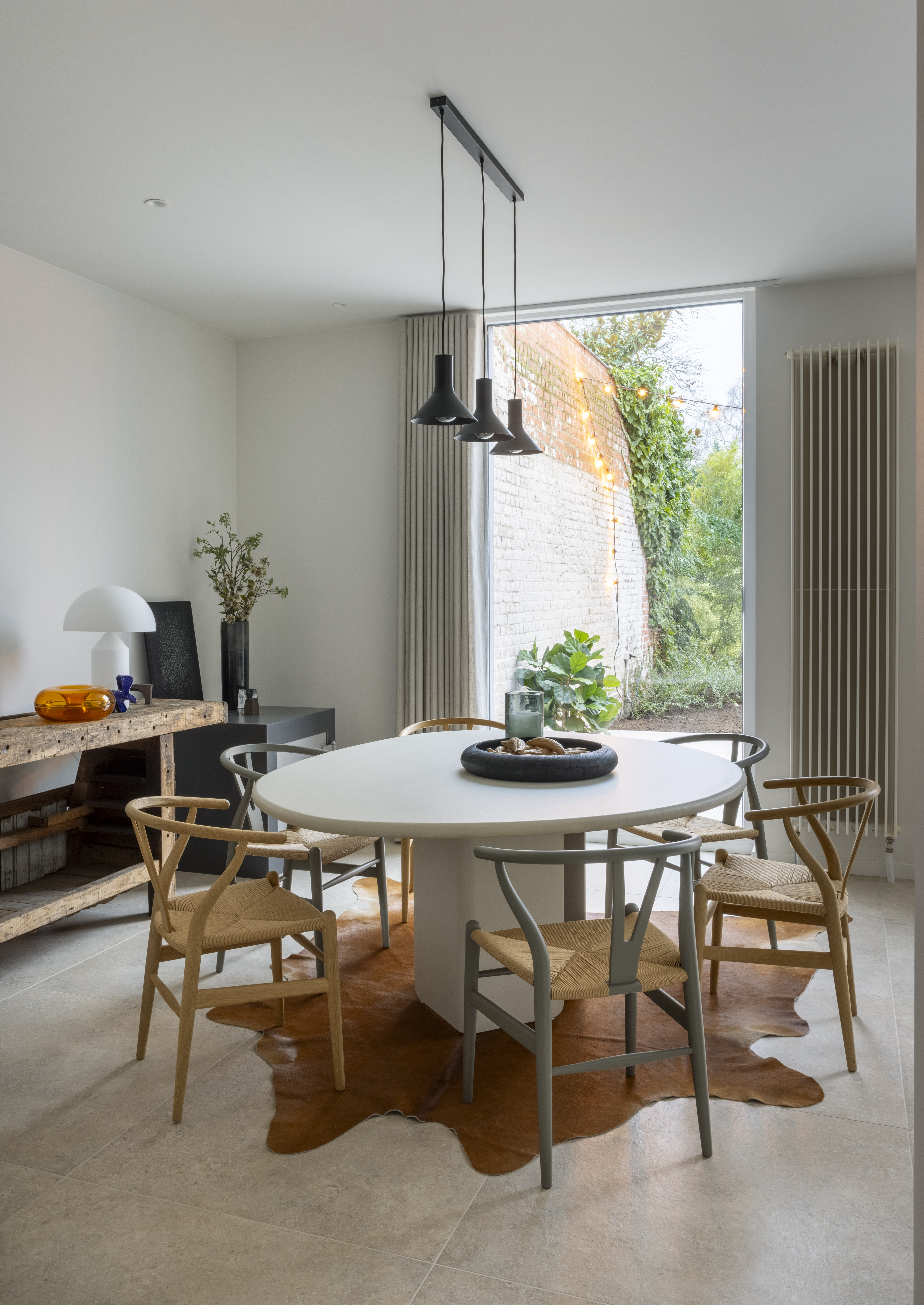 Modern eetgedeelte in een gerenoveerde gesloten bebouwing met een groot vast raam in witte raamprofielen, naast een bakstenen buitenmuur.