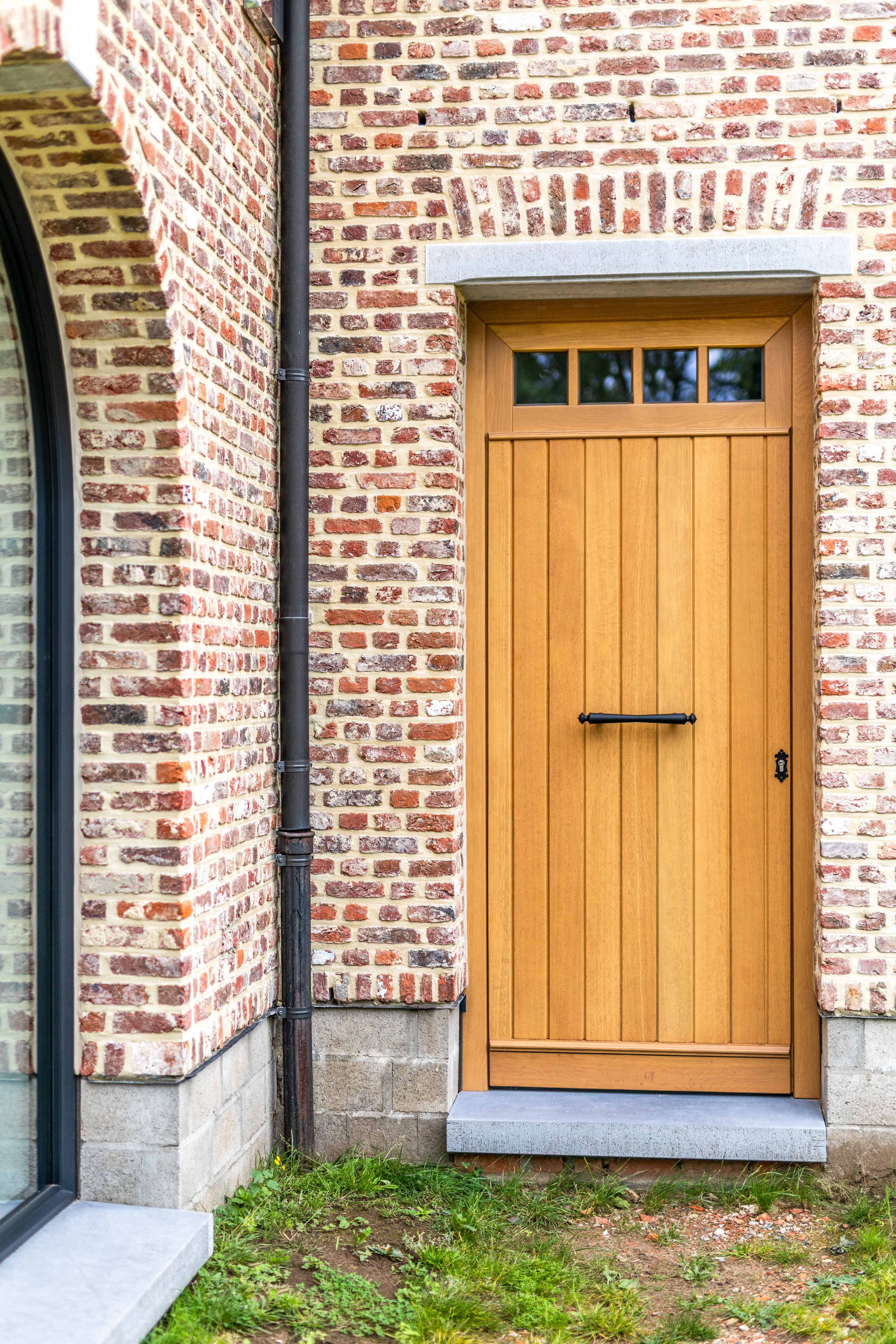 Afgelakte mahoniehouten voordeur met bovenlicht in een warme landelijke stijl, geplaatst in een karaktervolle bakstenen gevel van een vrijstaande woning.