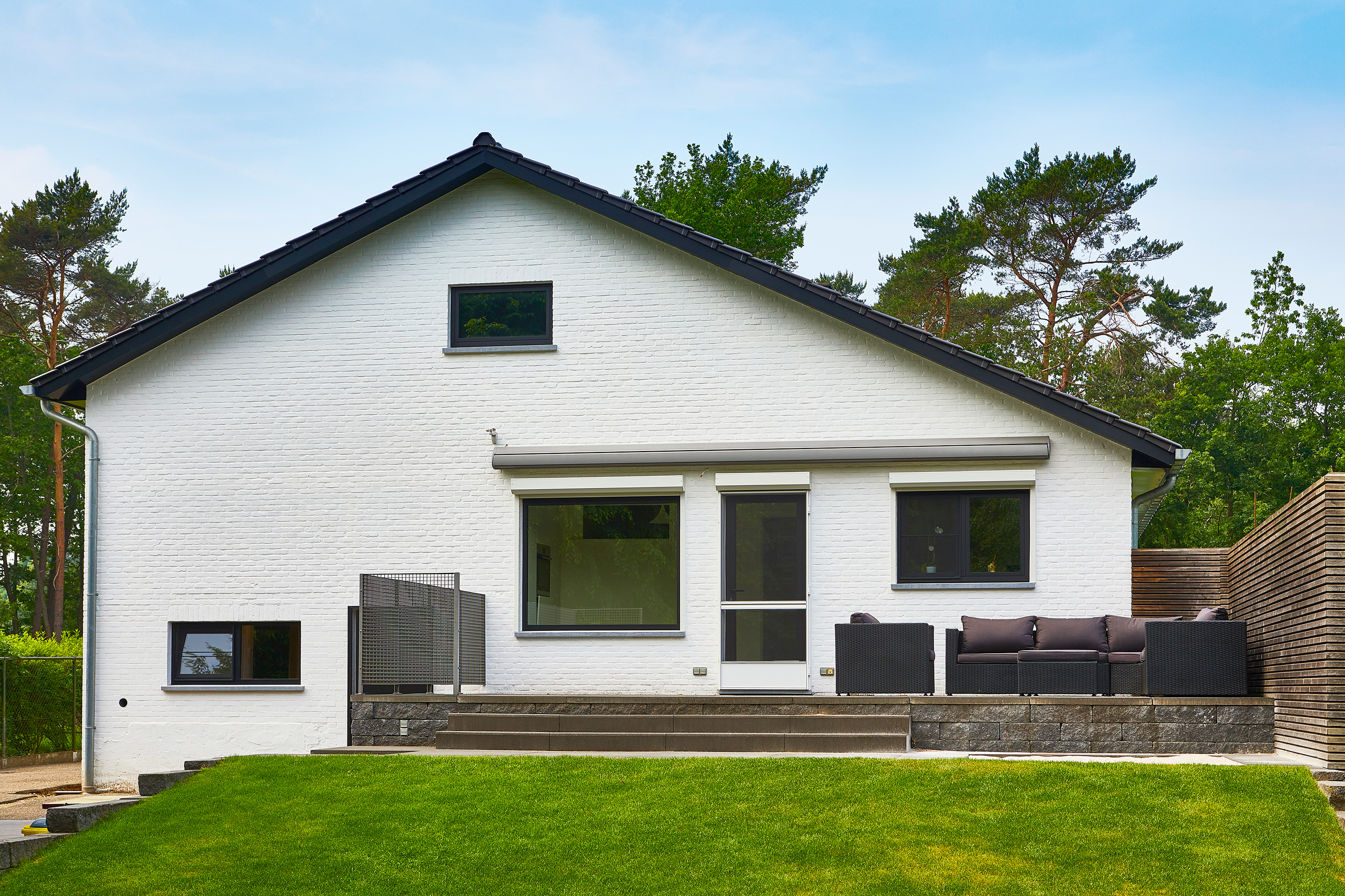 Gerenoveerde open bebouwing met witte gevel, zwarte steellook raamprofielen en deur, en een gezellig terras in een groene omgeving.