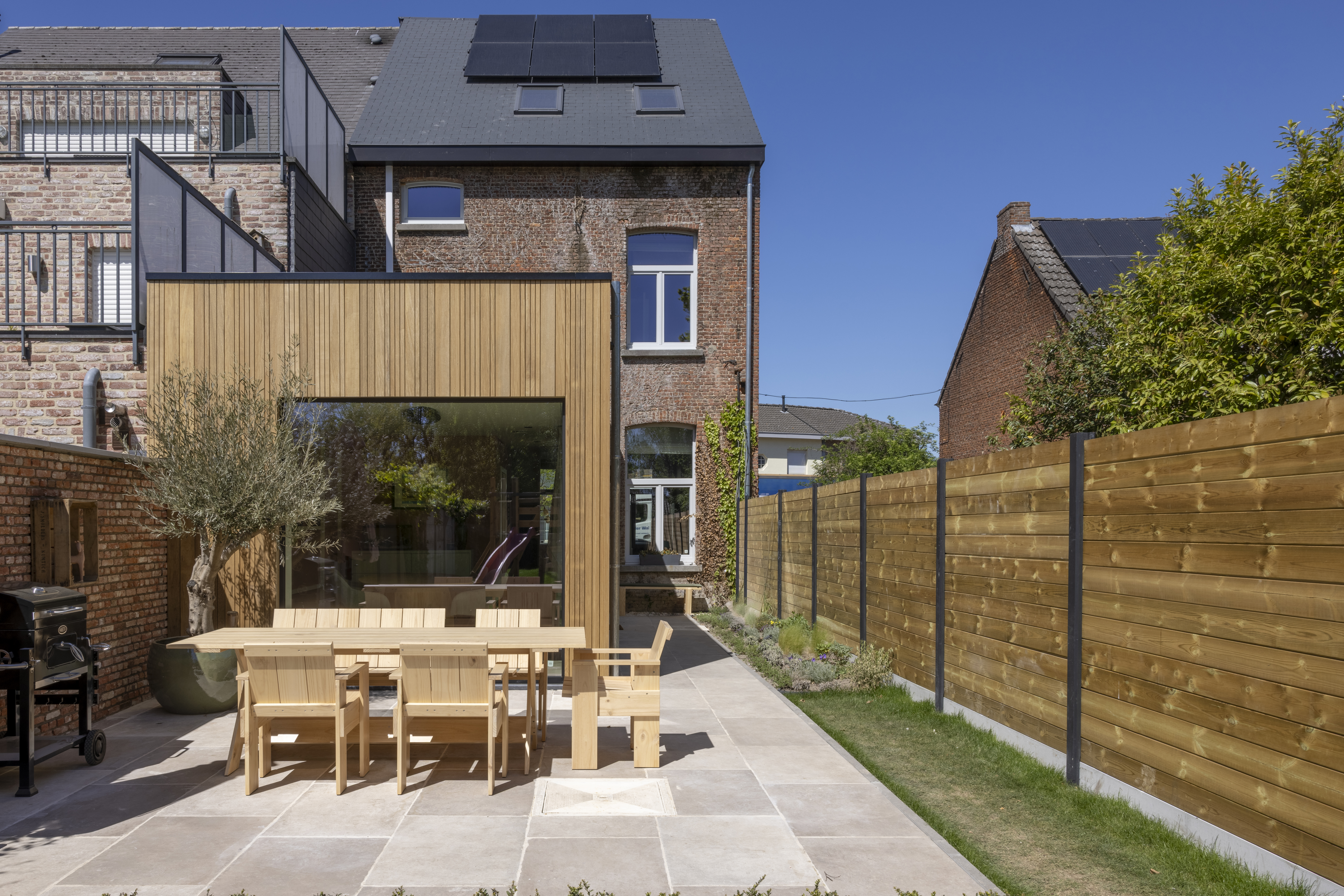 Vast raam Komfort EVO small in 9004TC signaalzwart, geïntegreerd in een moderne houten gevelbekleding aan een bakstenen gevel met terras en tuin.