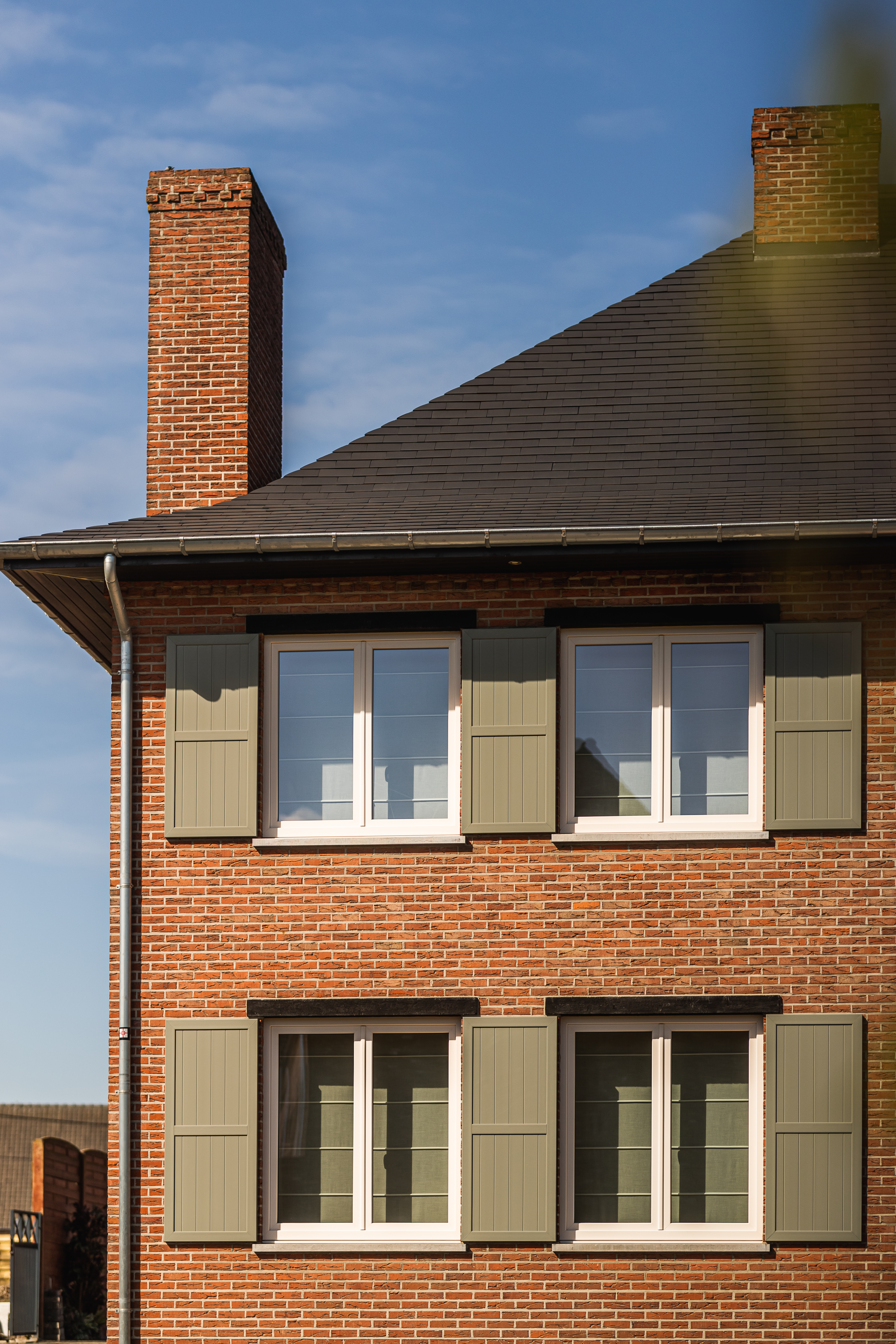 Gerenoveerde vrijstaande bakstenen woning met crème dubbele ramen in een gemoedelijke, tijdloze stijl en groene klapluiken aan de gevel.
