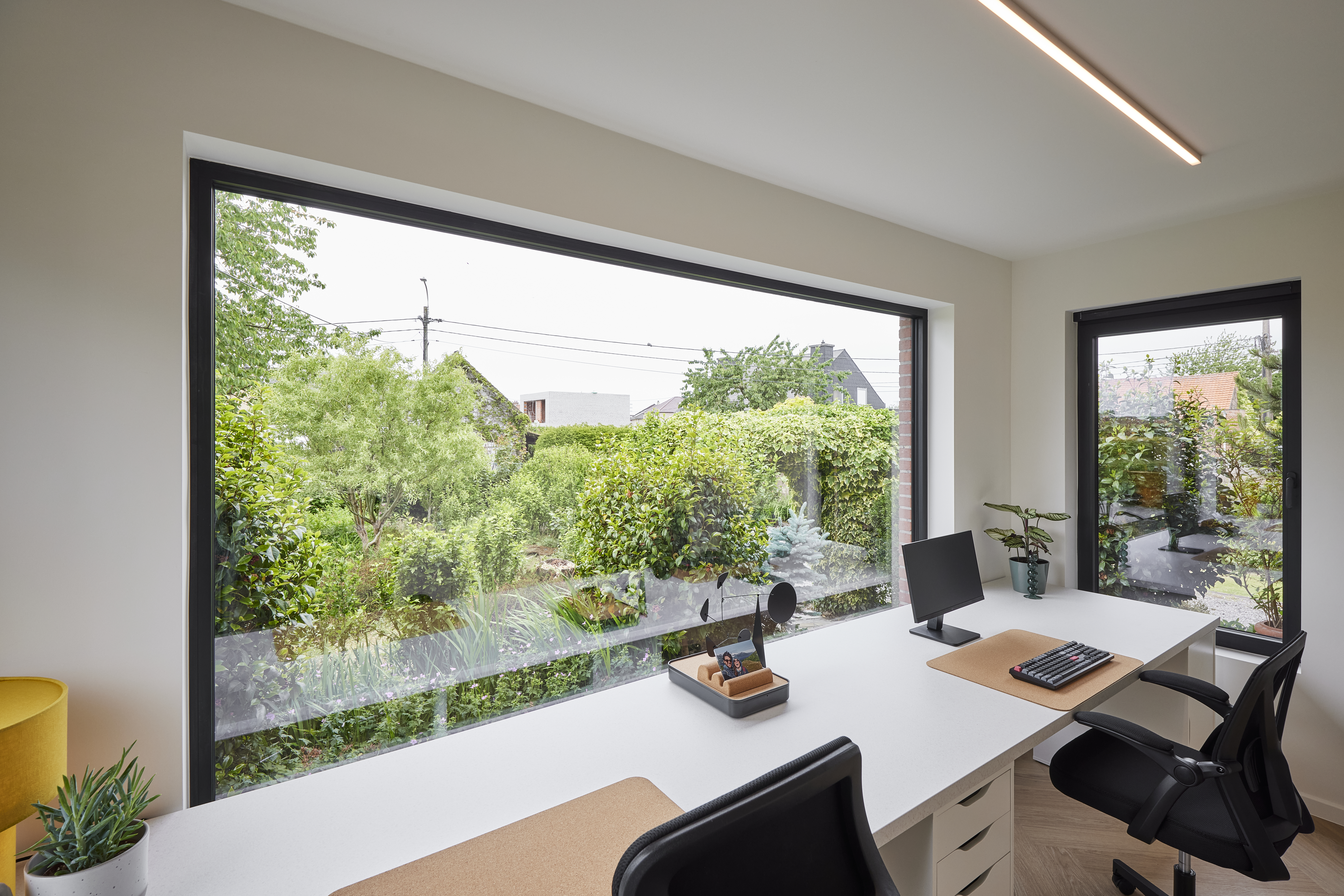 Licht interieur met een groot vast raam en een draai-kipraam uit de Komfort EVO small-reeks, met grafietzwarte raamprofielen en uitzicht op een groene tuin.