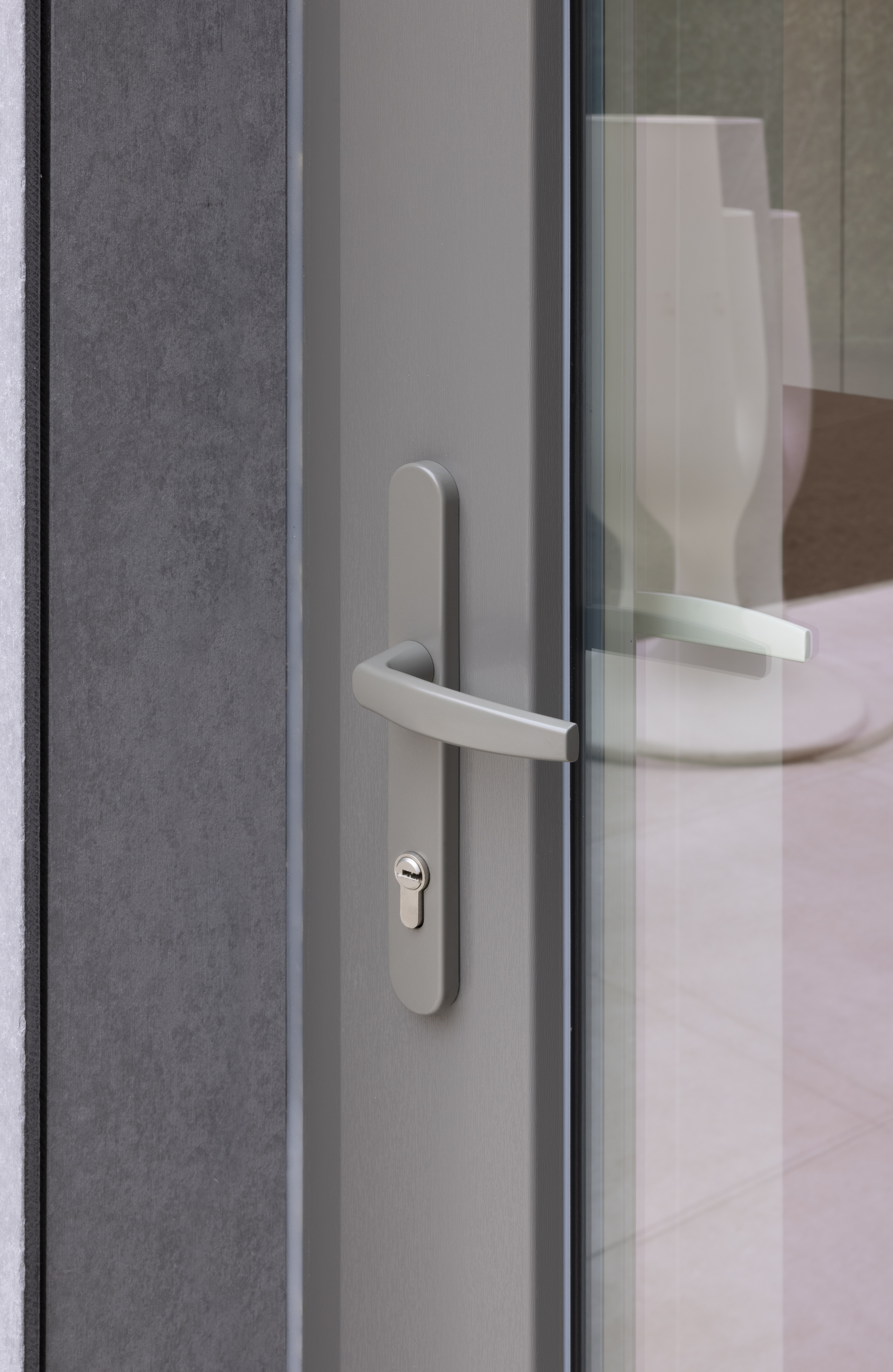 Moderne beglaasde deur met kwartsgrijs PVC-profiel, slanke glaspartij en horizontale metalen deurkruk, passend bij renovatie in gesloten bebouwing.