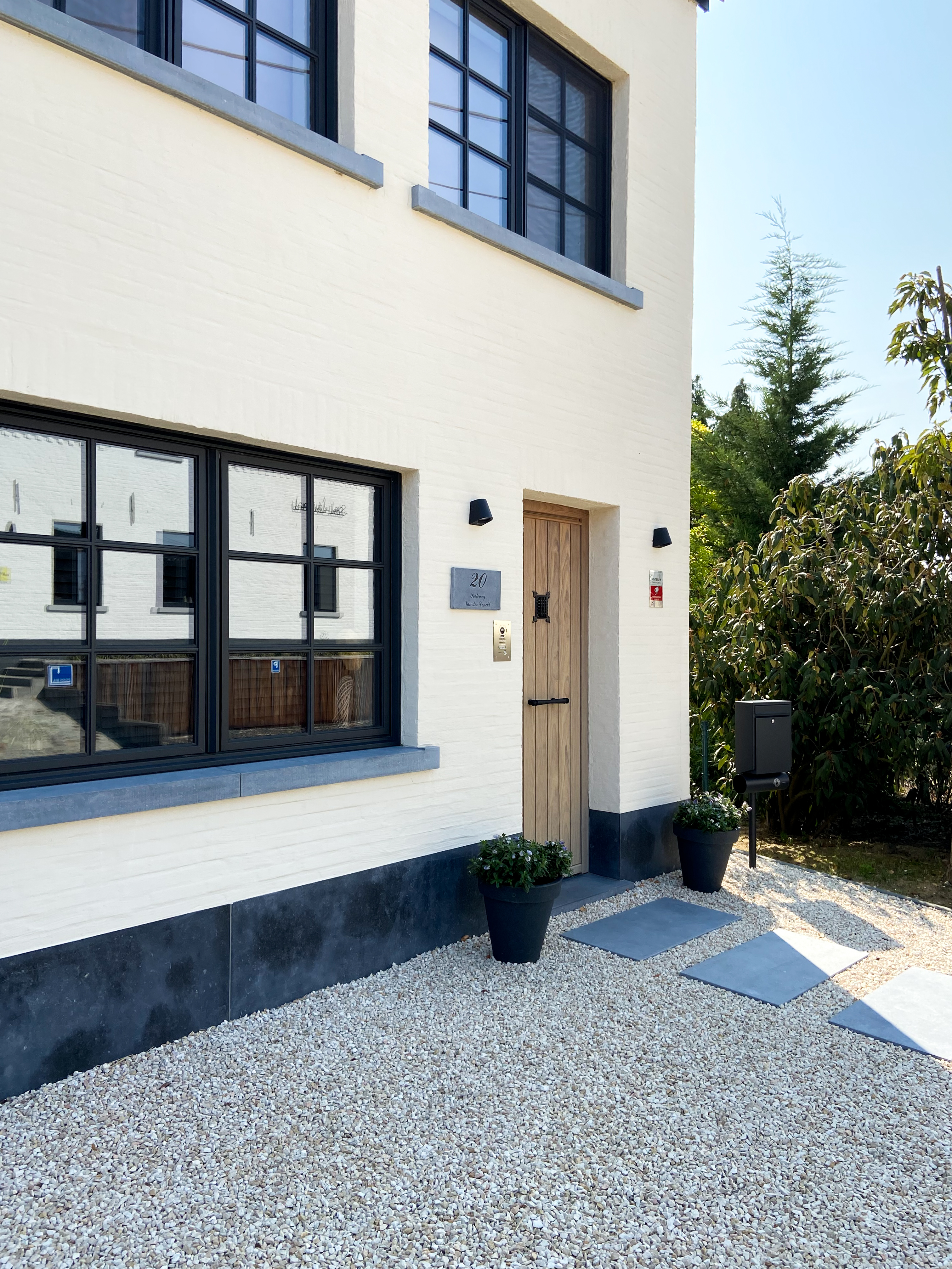 Witte gevel van een vrijstaande, gerenoveerde woning met zwarte Steellook PLUS small-profielen, een dubbel raam en een draai-kipraam in warme landelijke stijl.