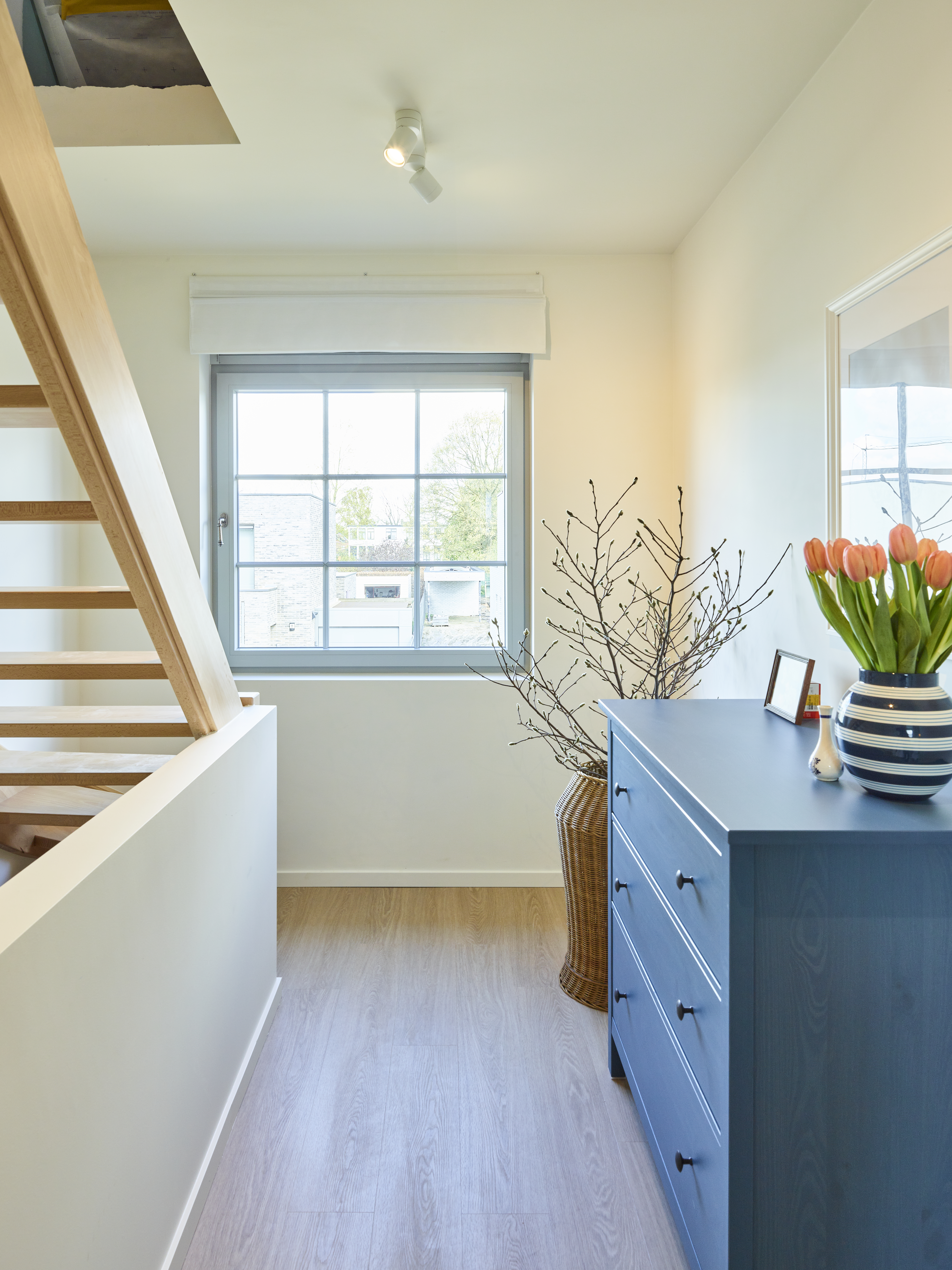Agaatgrijs draai-kipraam met steellook in een warm landelijk interieur, naast een trap en blauw dressoir, met natuurlijk daglicht en Komfort PLUS.