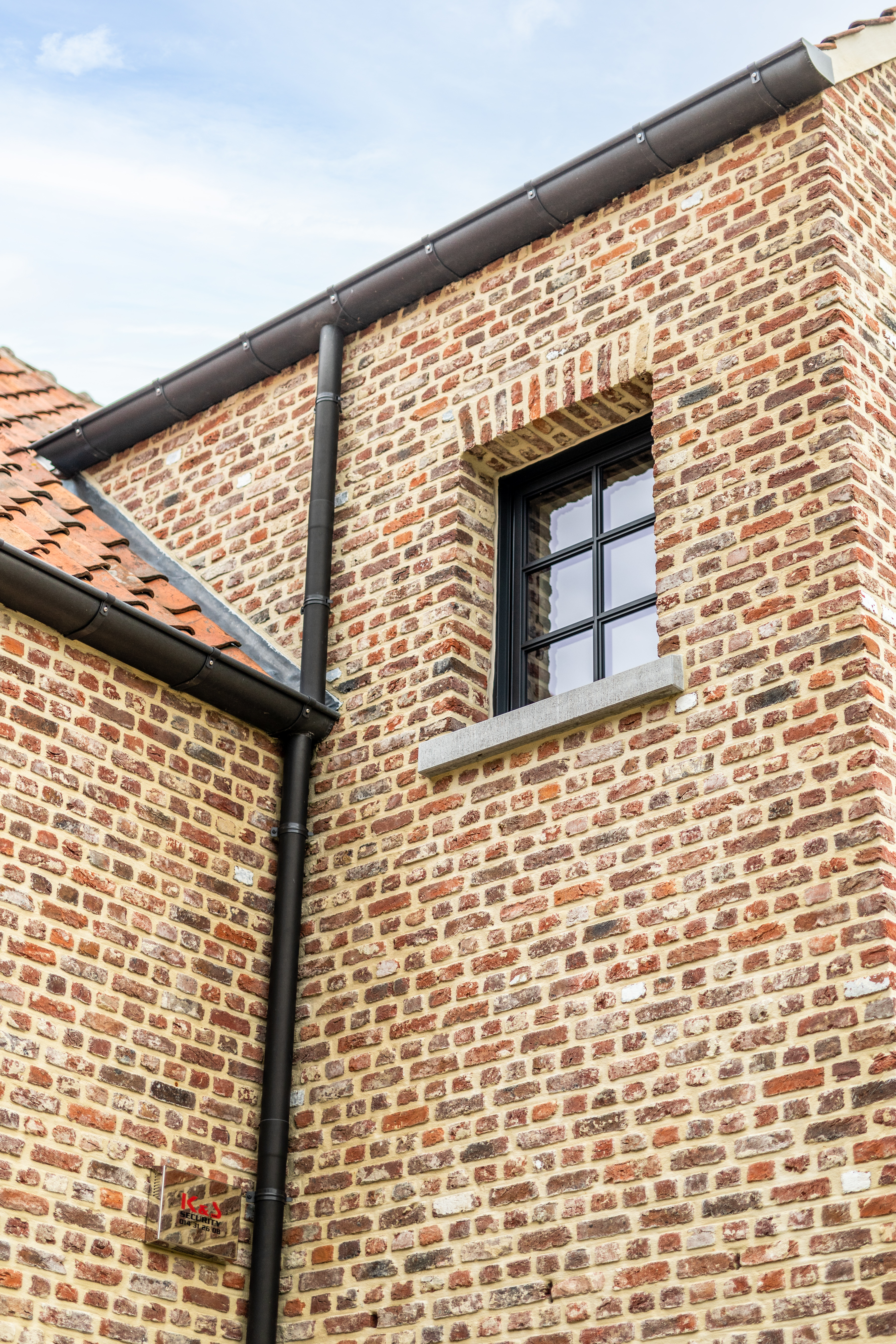 Zwart Steellook PLUS draai-kipraam in een warme, landelijke bakstenen gevel van een open bebouwing, onder een donkere dakrand.