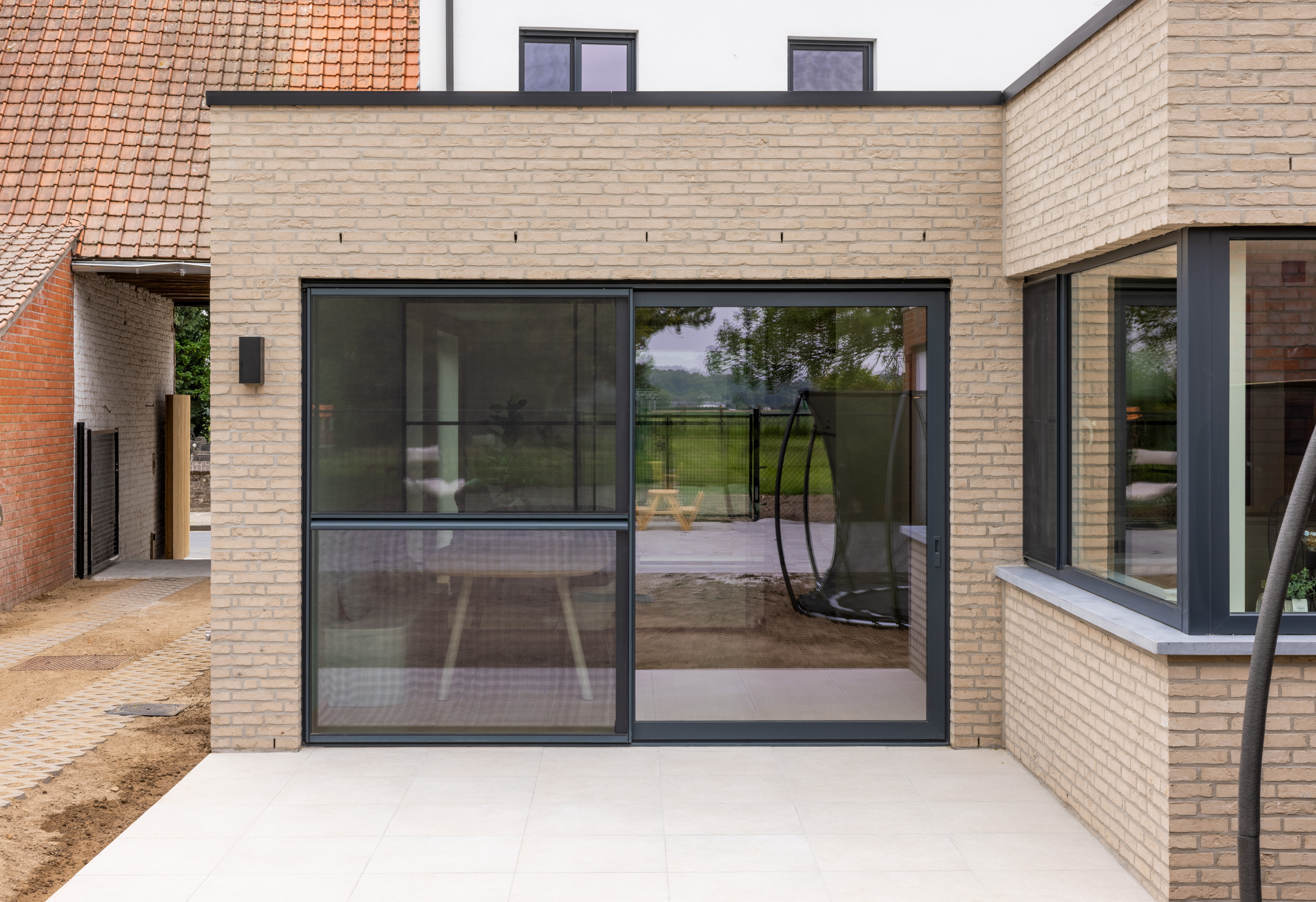 Moderne achtergevel van een gerenoveerde gesloten bebouwing met een antracietgrijs ALU Visoglide Monorail-schuifraam en schuifvliegenraam, naast een hoekraam.