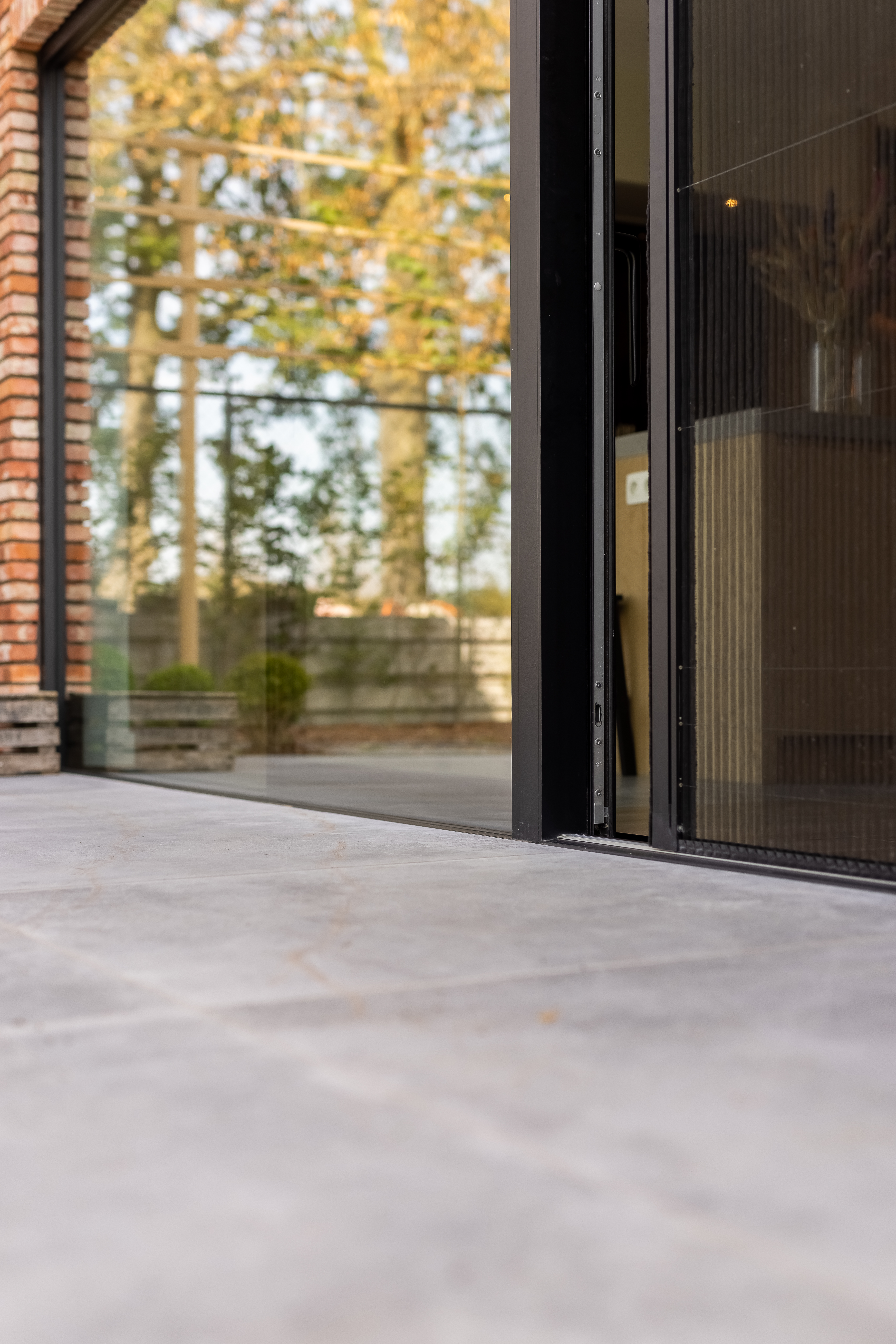 Zwart aluminium schuifraam met plisséhor in een warm landelijke nieuwbouwwoning, met zicht op de bosrijke omgeving.