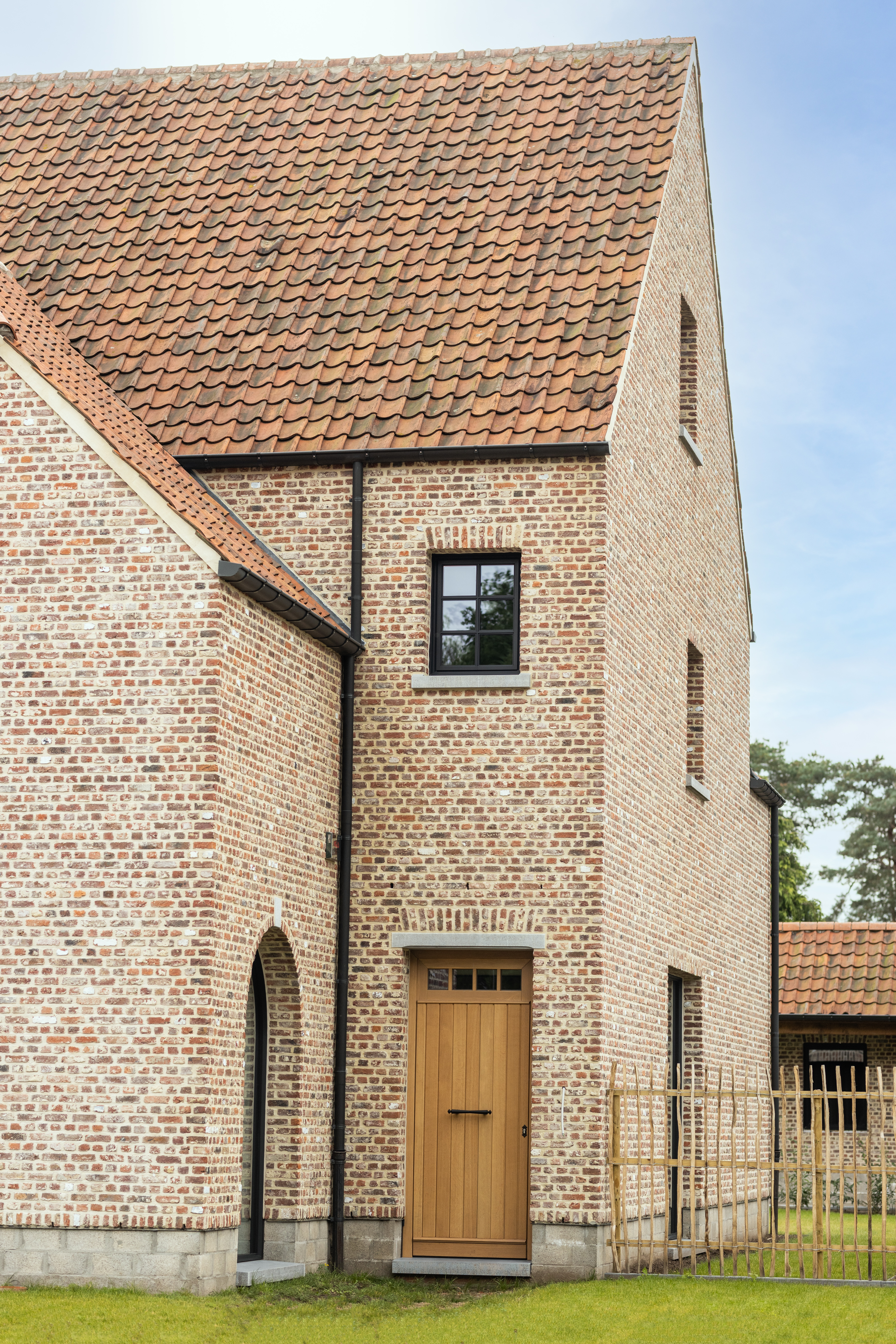 Landelijke bakstenen woning met een houten deur en zwart Steellook PLUS-bovenlicht in de gevel, passend bij een nieuwbouwproject in open bebouwing.