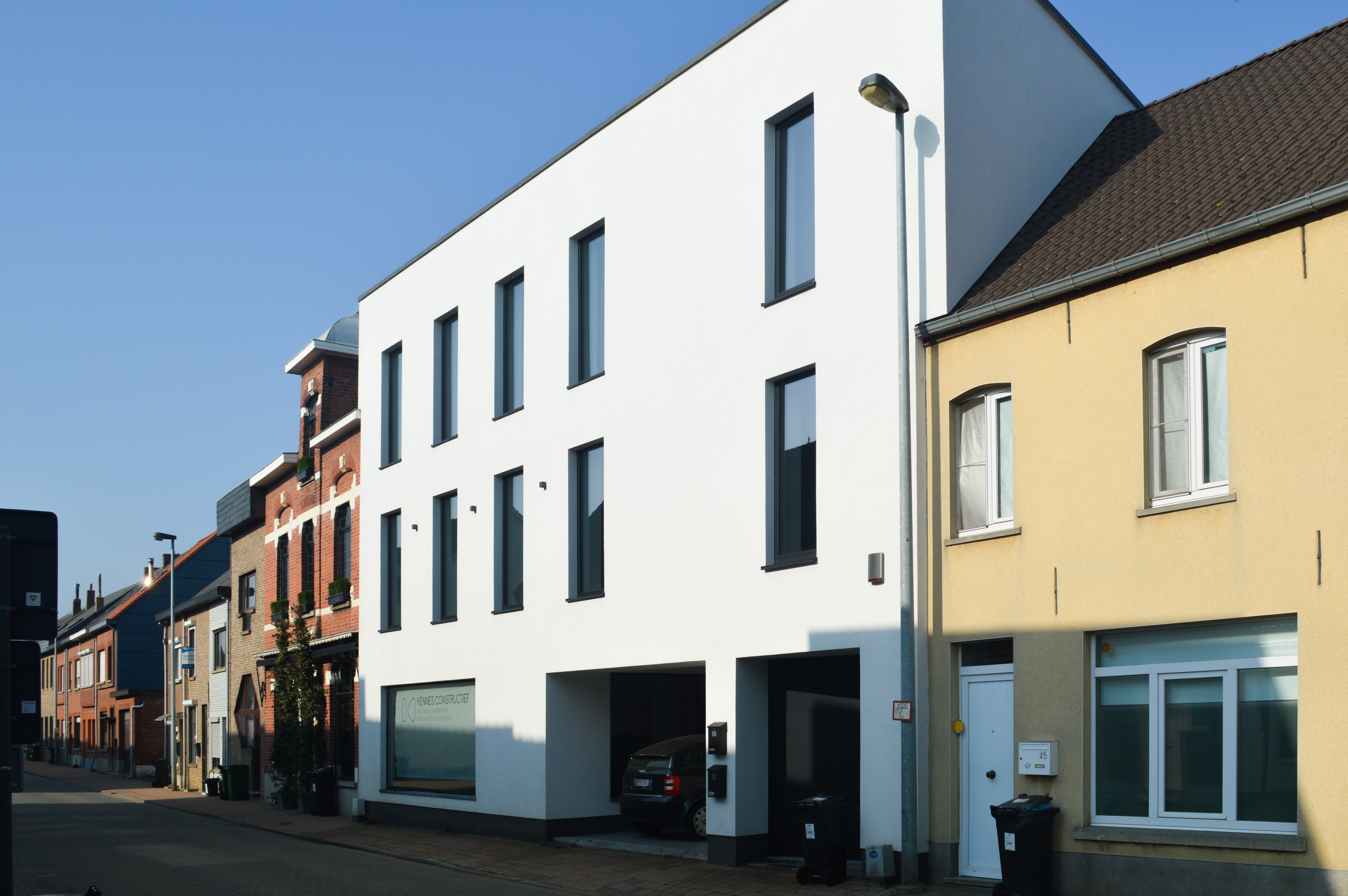 Moderne witte gevel met zwarte Koncept-raamprofielen in 9005TC, naast oudere rijhuizen langs een straat.
