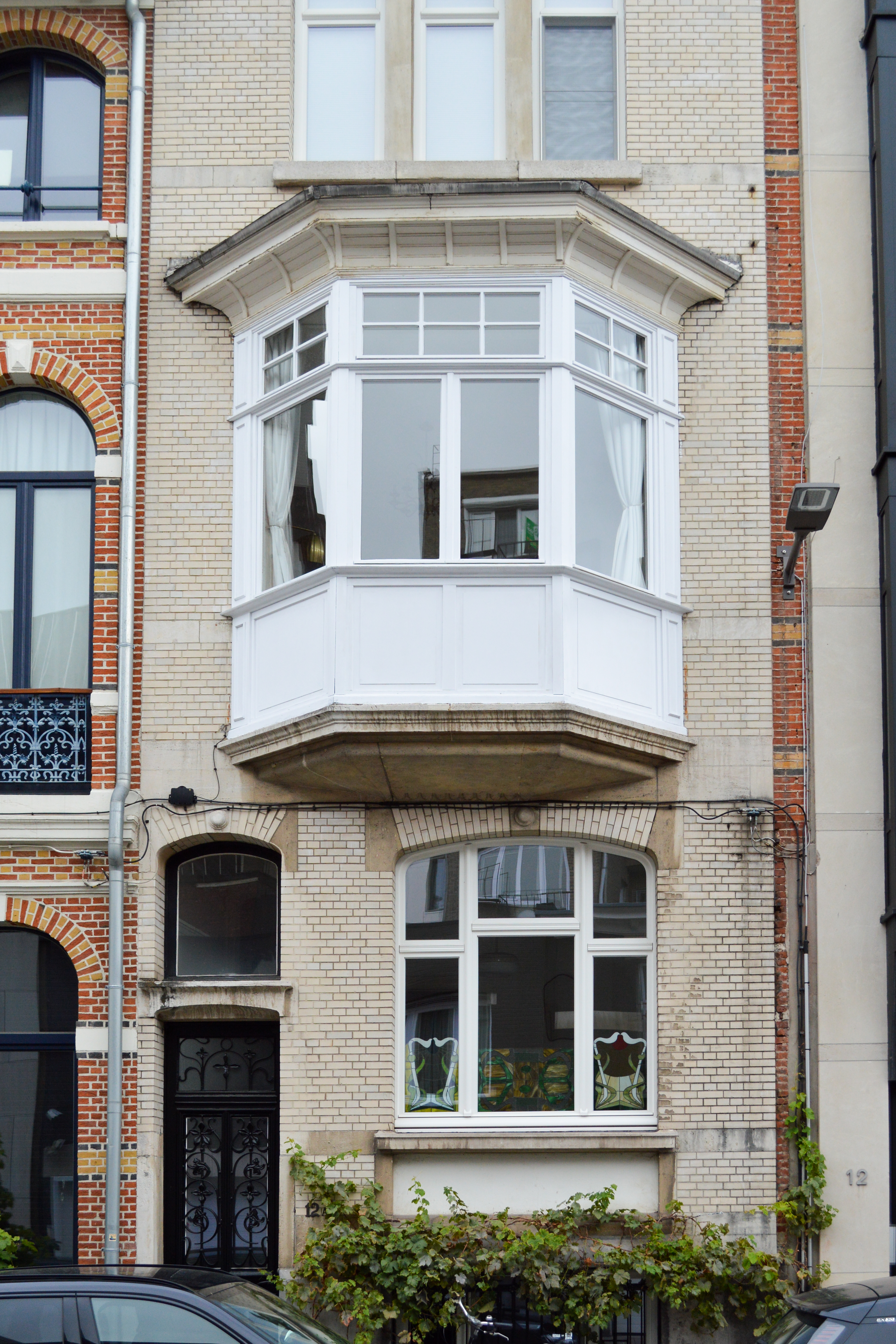 Klassieke bakstenen gevel met een wit afgelakt erkerraam, gecombineerd met draai-kipramen en ramen met boven- en onderlicht in gesloten bebouwing.