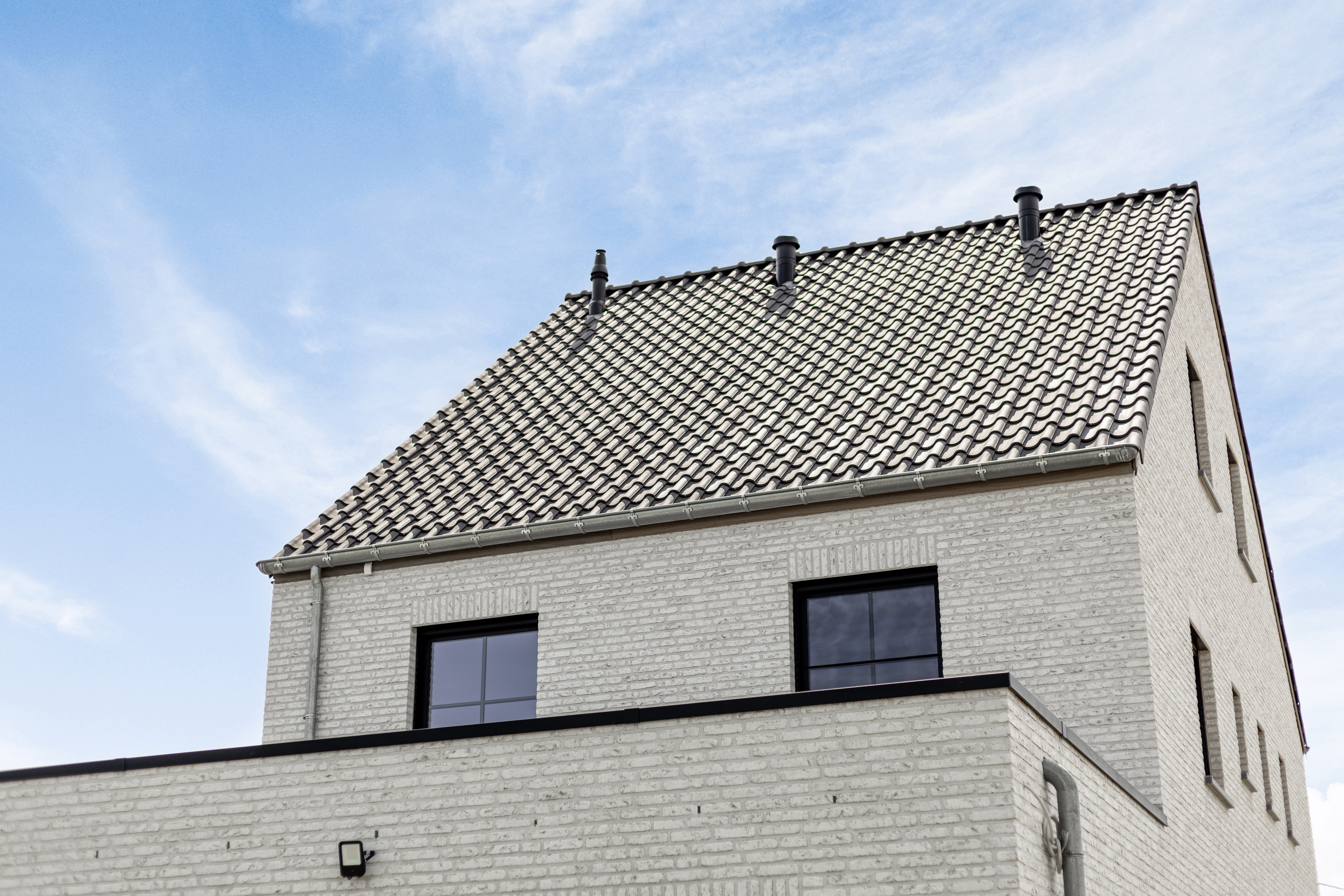 Vrijstaande woning in een warme landelijke stijl, met lichte bakstenen, signaalzwarte raamprofielen en een hellend pannendak.