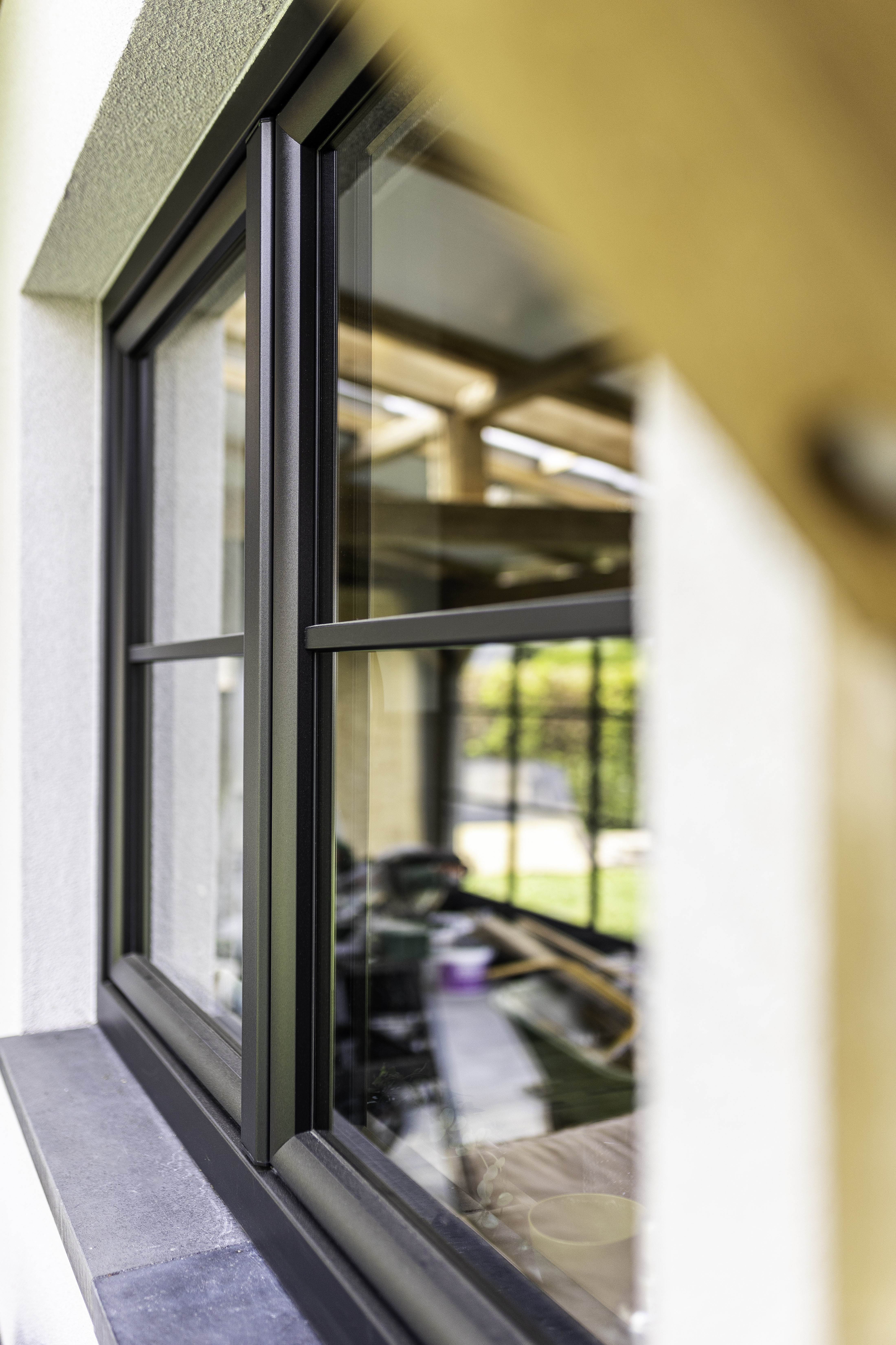 Mat zwart draai-kipraam met dubbele beglazing in een lichte gevel, gedeeltelijk geopend met zicht op het interieur.