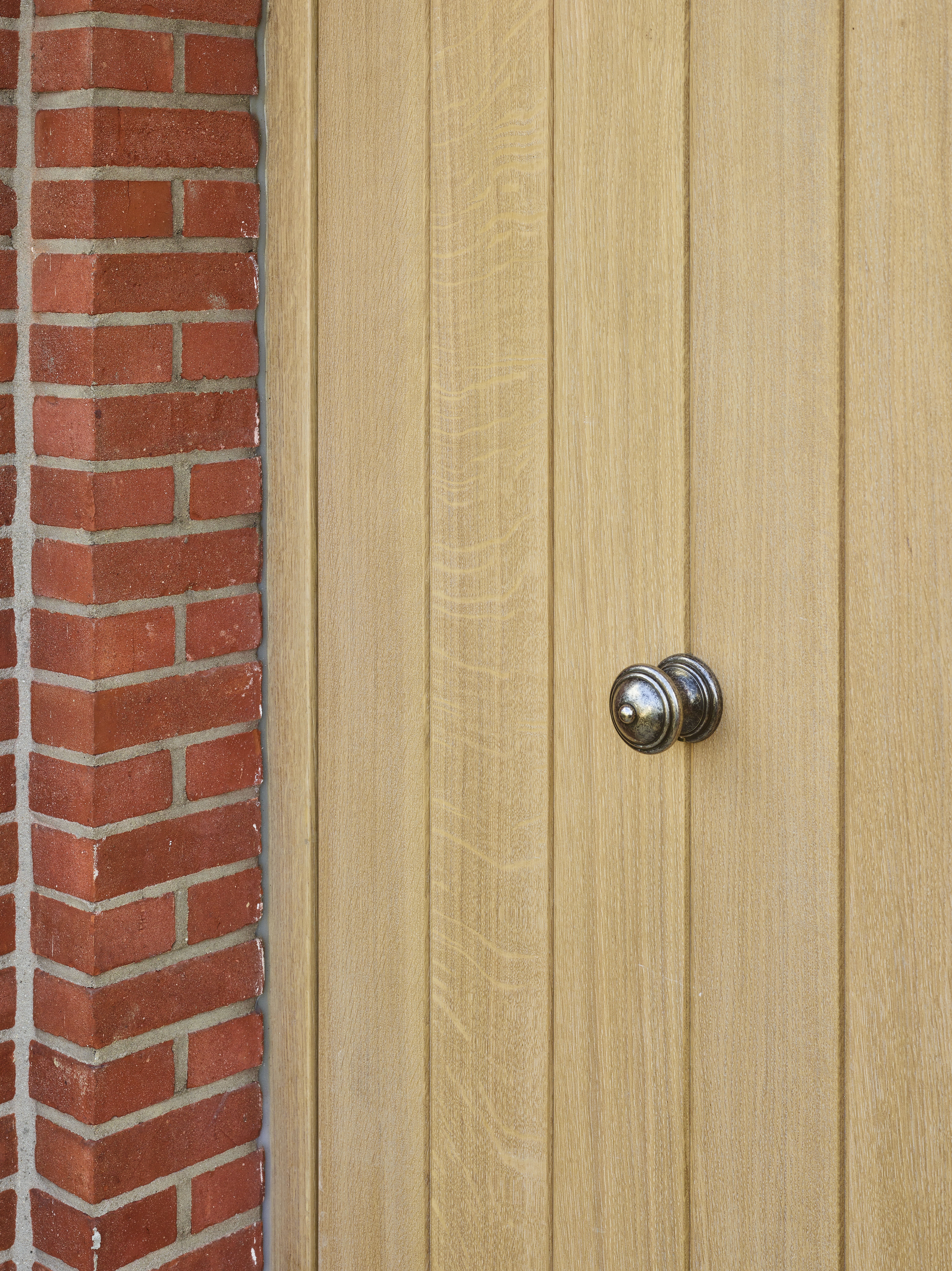 Afgewerkt paneel in lichte eik naast een rode bakstenen muur, met een ronde metalen knop en een warme, landelijke uitstraling.