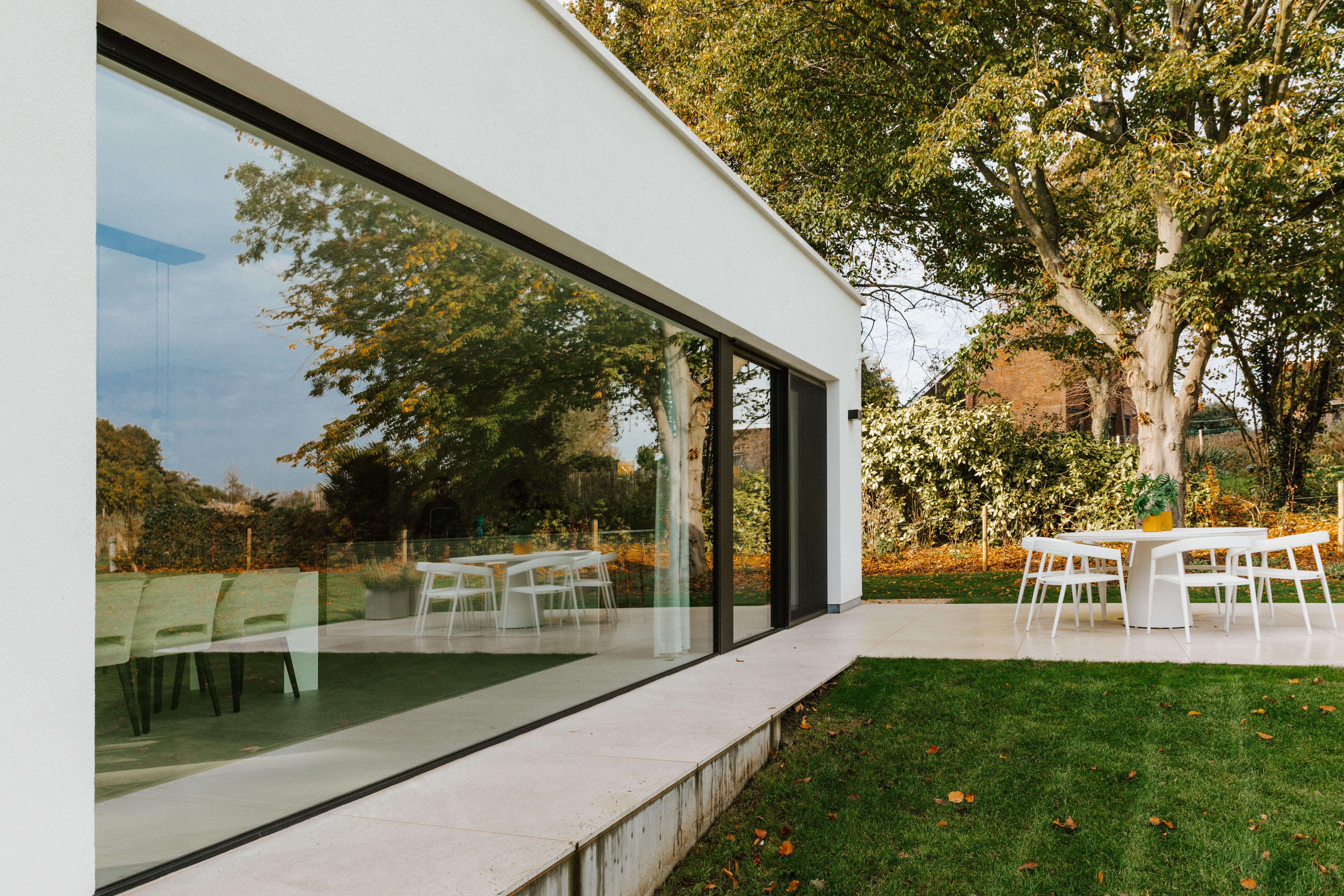 Grande fenêtre fixe aux profils en aluminium noir dans une habitation moderne rénovée quatre façades, donnant sur la terrasse, le jardin et la salle à manger.