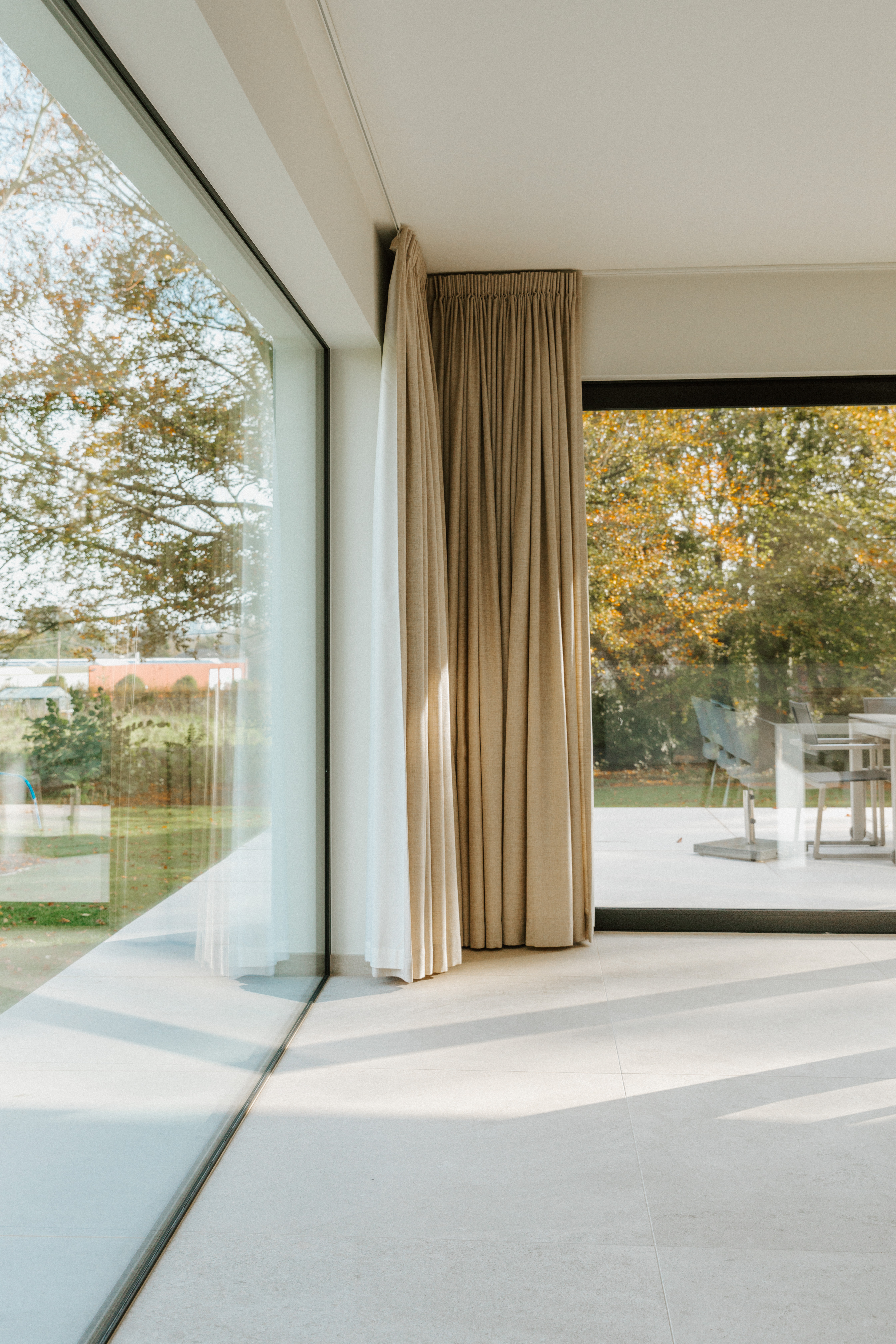 Modern vast raam met aluminiumprofielen in een gerenoveerde woning, naast een groot schuifraam met gordijnen en uitzicht op de tuin.