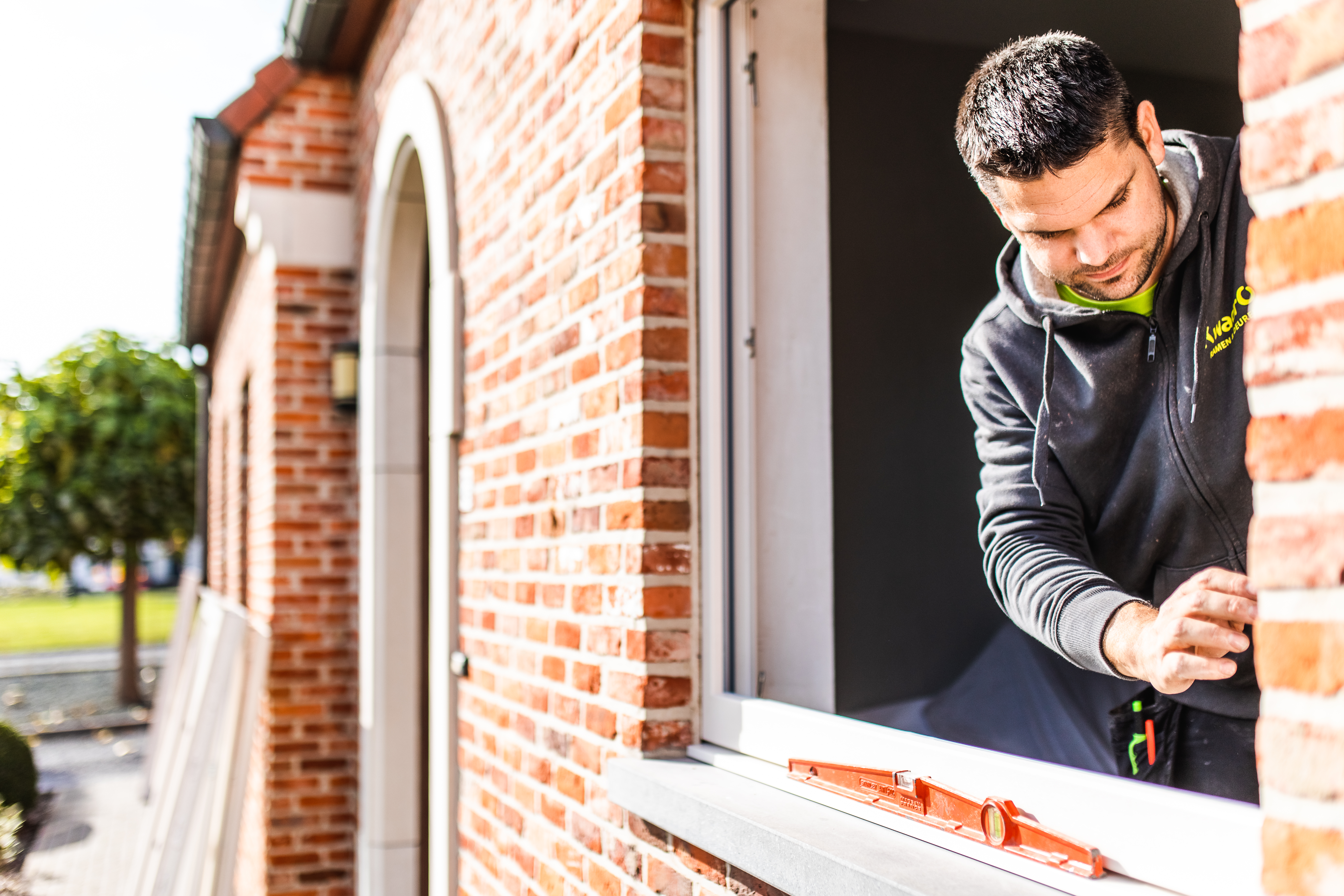Une personne travaille sur une fenêtre dans une façade en briques rouges et se penche vers l’extérieur depuis l’habitation.