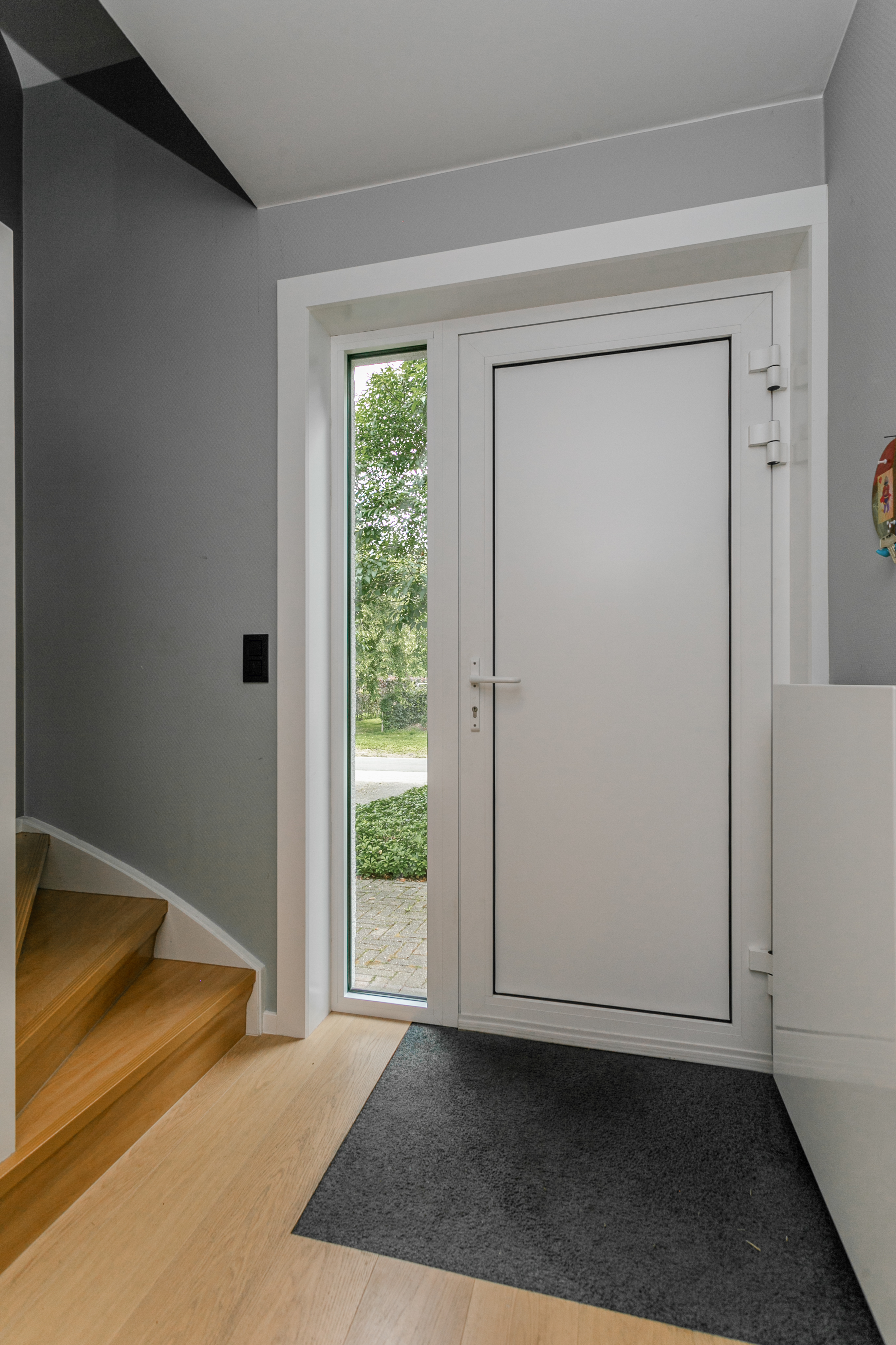 Witte aluminium voordeur met zijlicht in mat verkeerswit, geplaatst in een lichte inkomhal met houten vloer en deurmat.