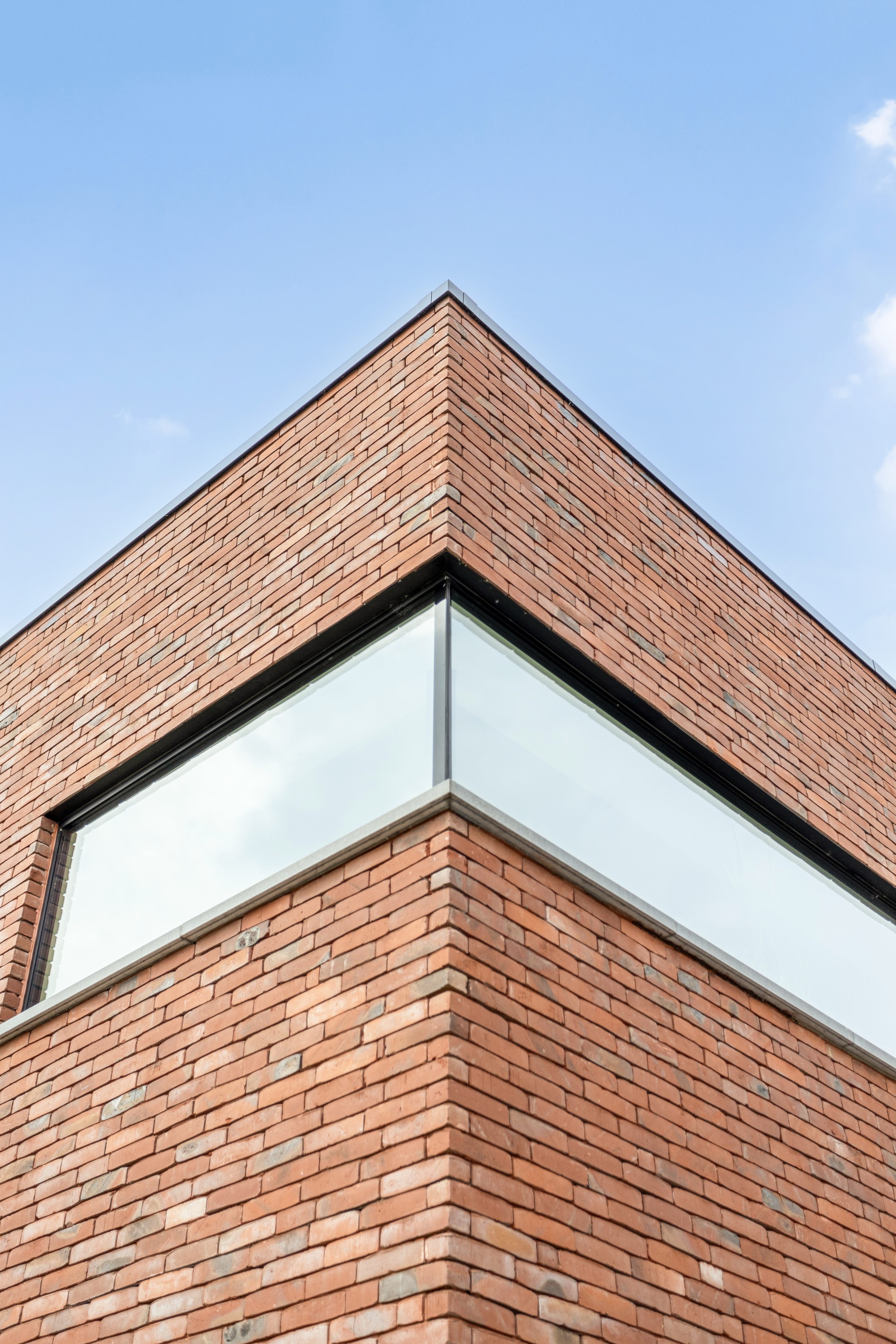 Modern hoekraam met zwarte raamprofielen in de hoek van een nieuwbouwwoning in baksteen, onder een blauwe hemel.