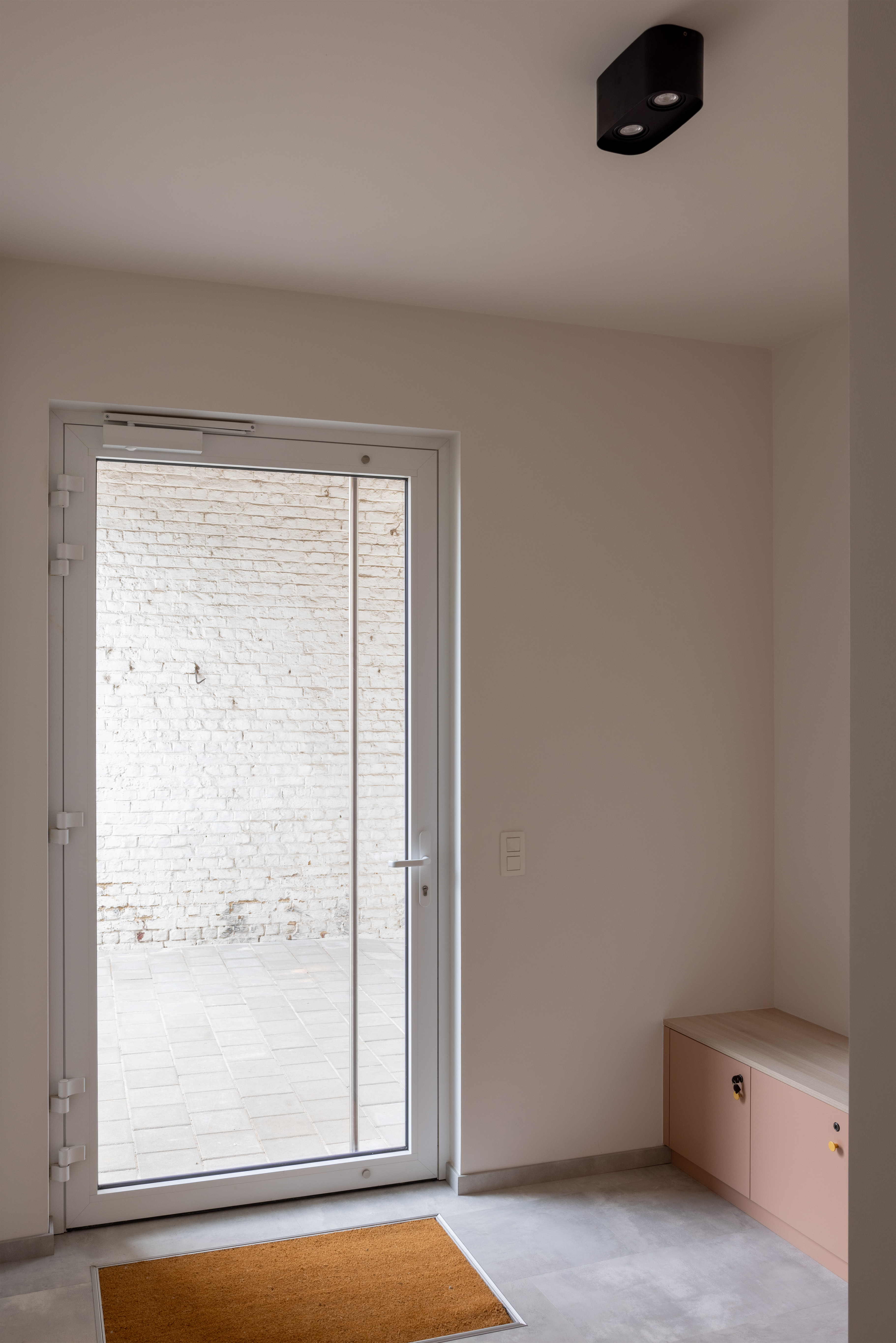 Moderne beglaasde aluminiumdeur in mat verkeerswit in een gerenoveerd interieur, met een klein meubelstuk ernaast.