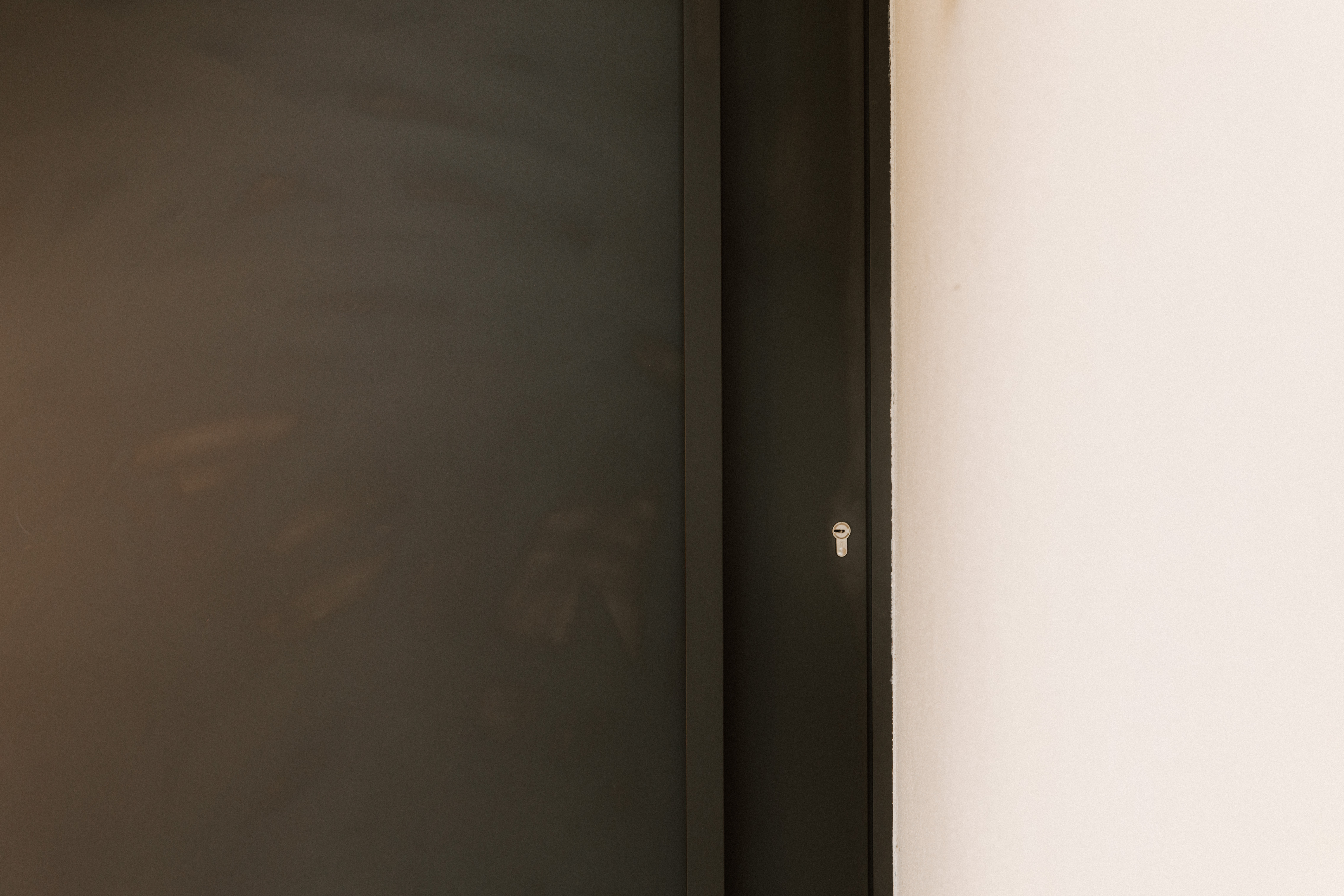 Close-up van een modern, signaalzwart aluminium paneel met smal raamprofiel en zichtbaar sleutelgat tegen een lichte wand.