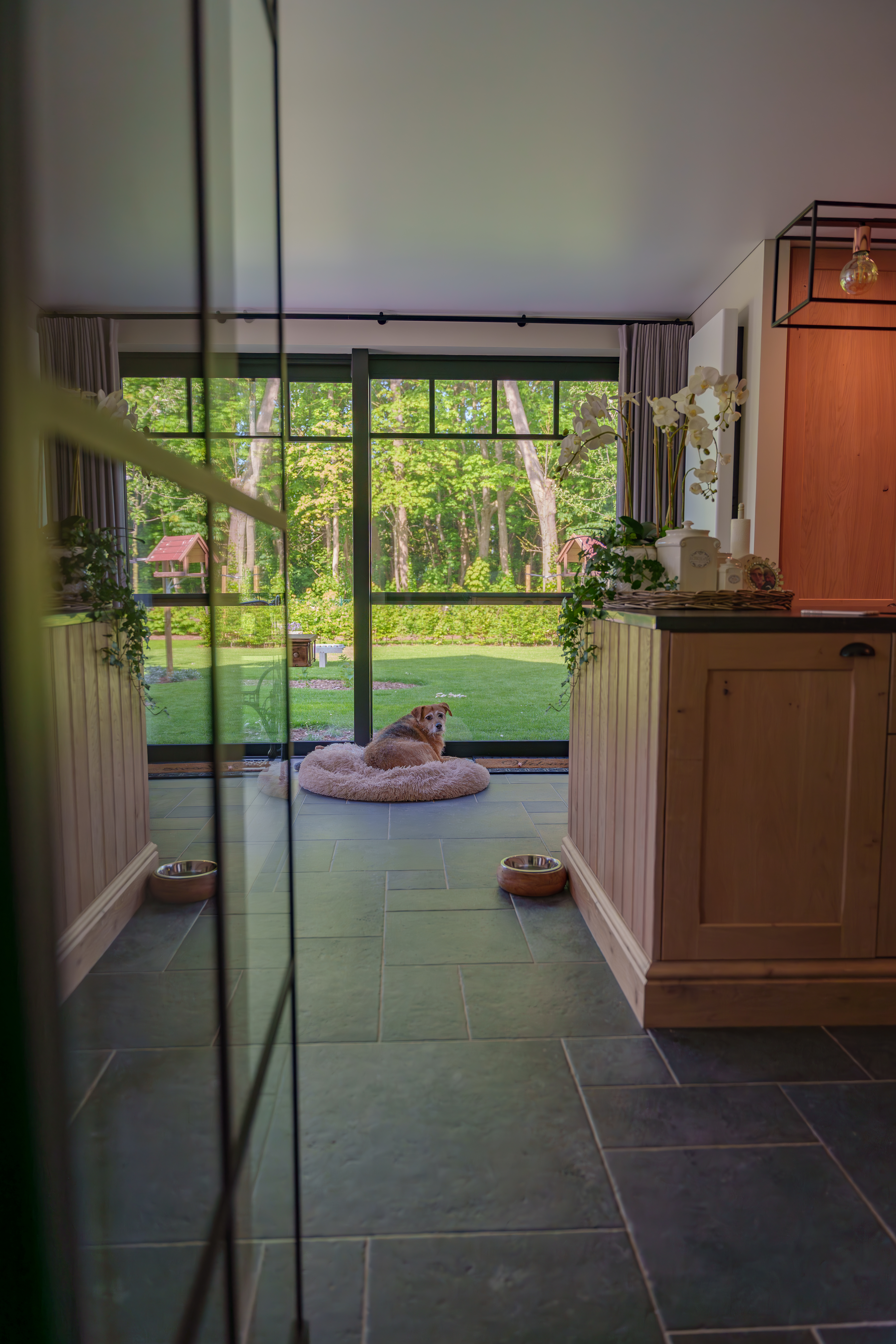 Mat zwart PVC Ekosol Duorail-schuifraam in een gerenoveerde, warm landelijke open bebouwing, met uitzicht op de groene tuin en het terras.