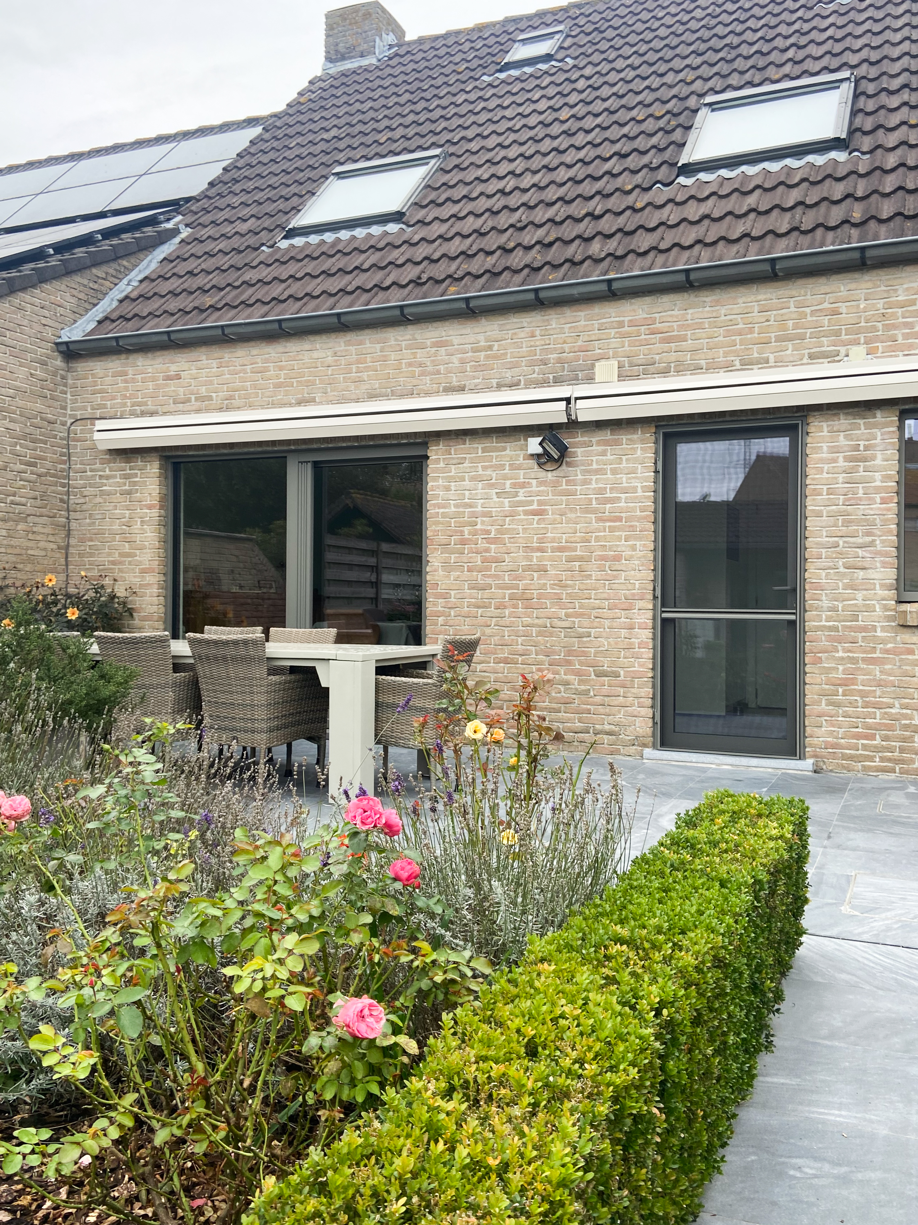 Gerenoveerde open bebouwing met tijdloze bakstenen gevel, dakramen, donkere raamprofielen, terras en verzorgde voortuin met buxushaag.