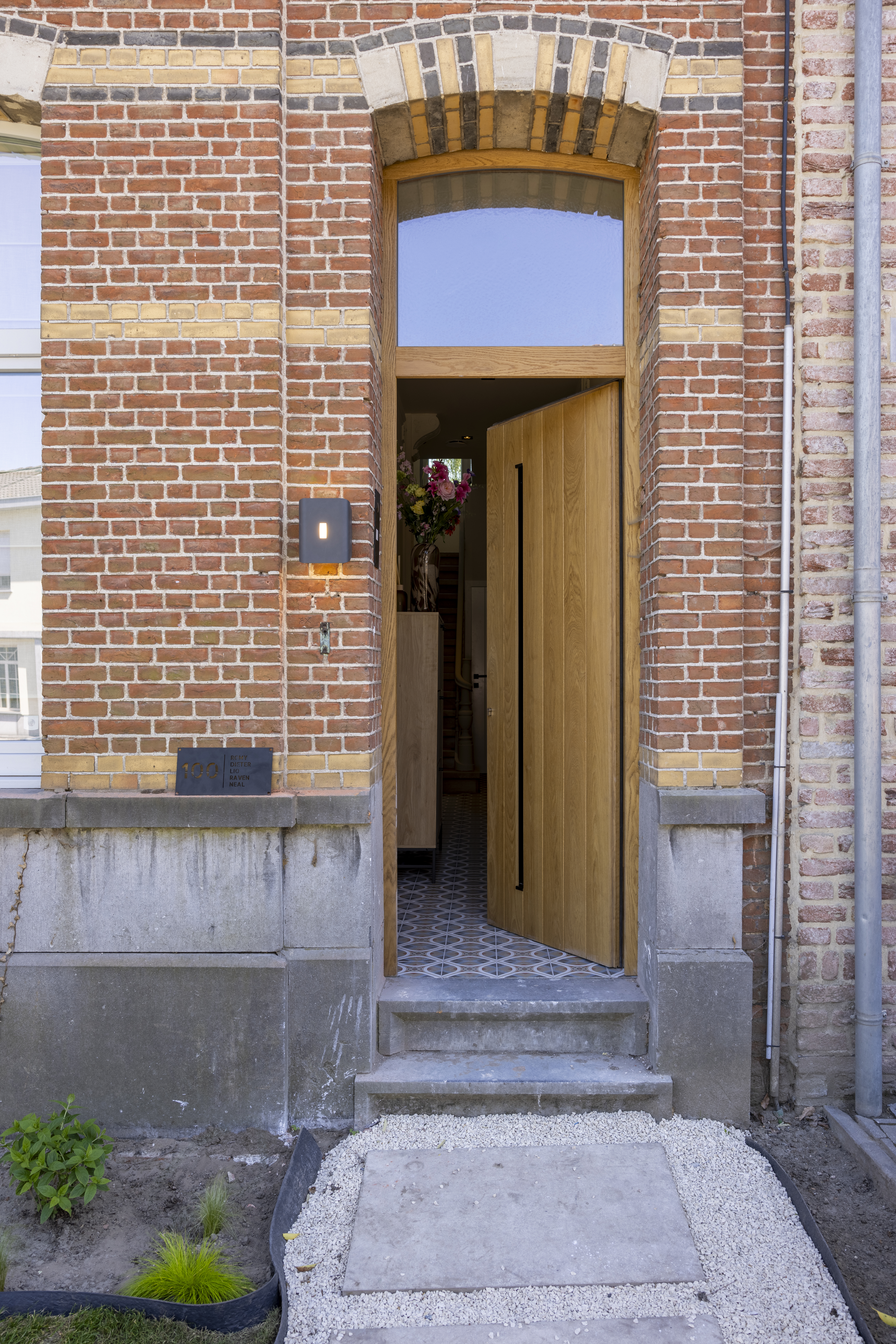 Eikenhouten deur met bovenlicht staat open in een smalle bakstenen gevel, met natuurstenen dorpel en zicht op de inkomhal.