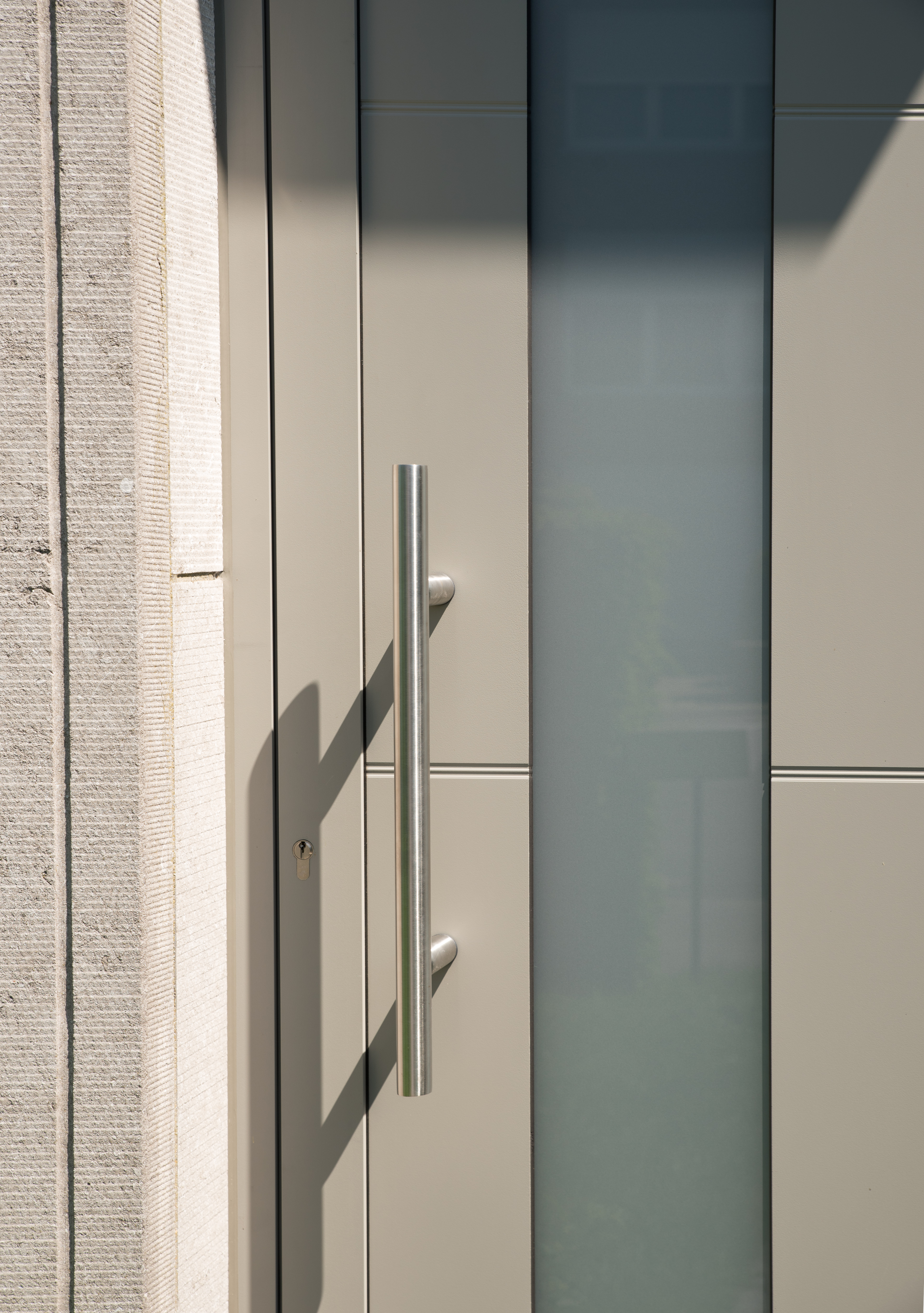 Close-up van een moderne, halfbeglaasde buitendeur met verticale handgrepen, geplaatst in een gerenoveerde gevel van een driegevelwoning.