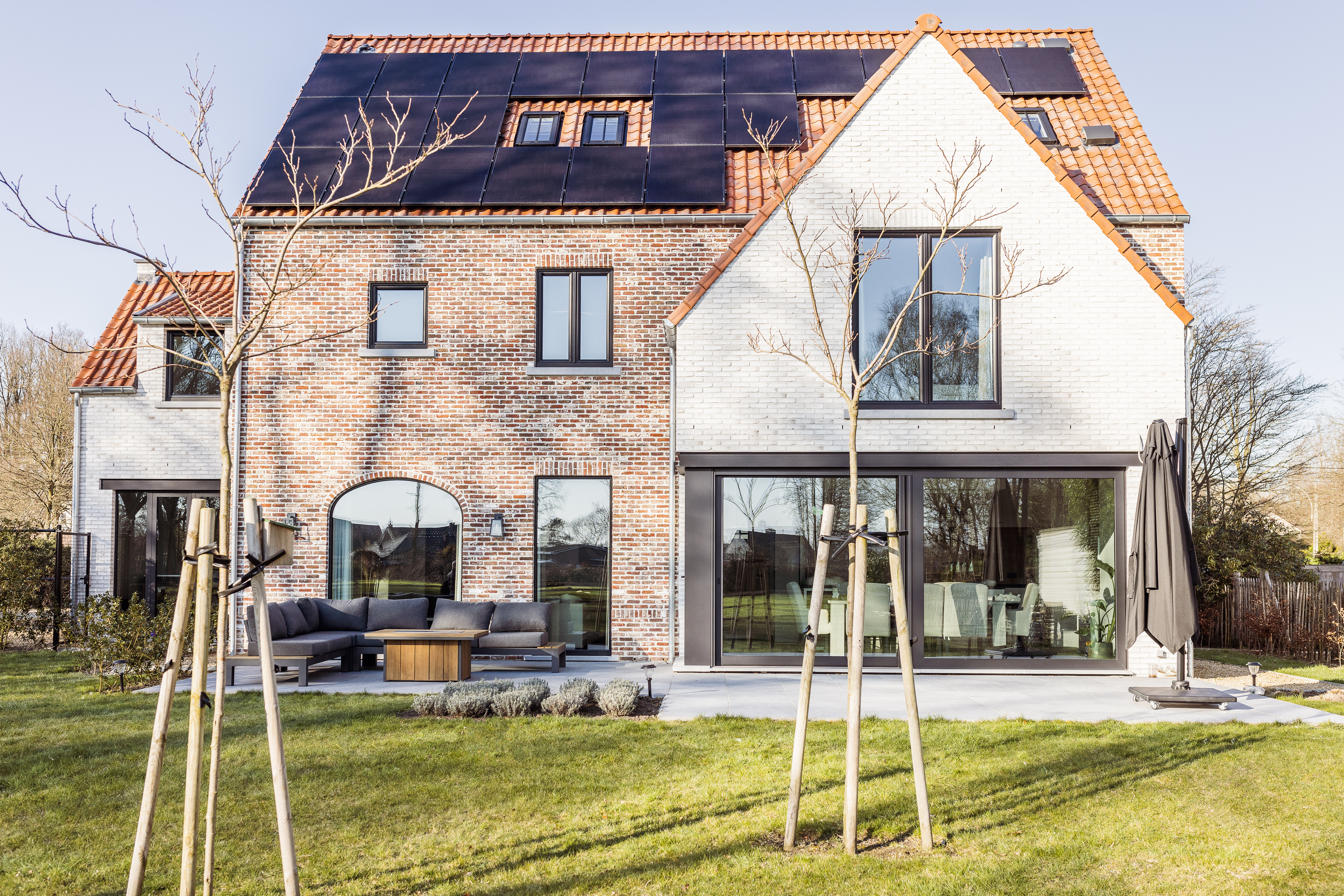 Moderne bakstenen woning met matzwarte aluminiumramen, een grote ALU Visoglide Duorail-schuifraam en draai-kipramen aan de tuinzijde.