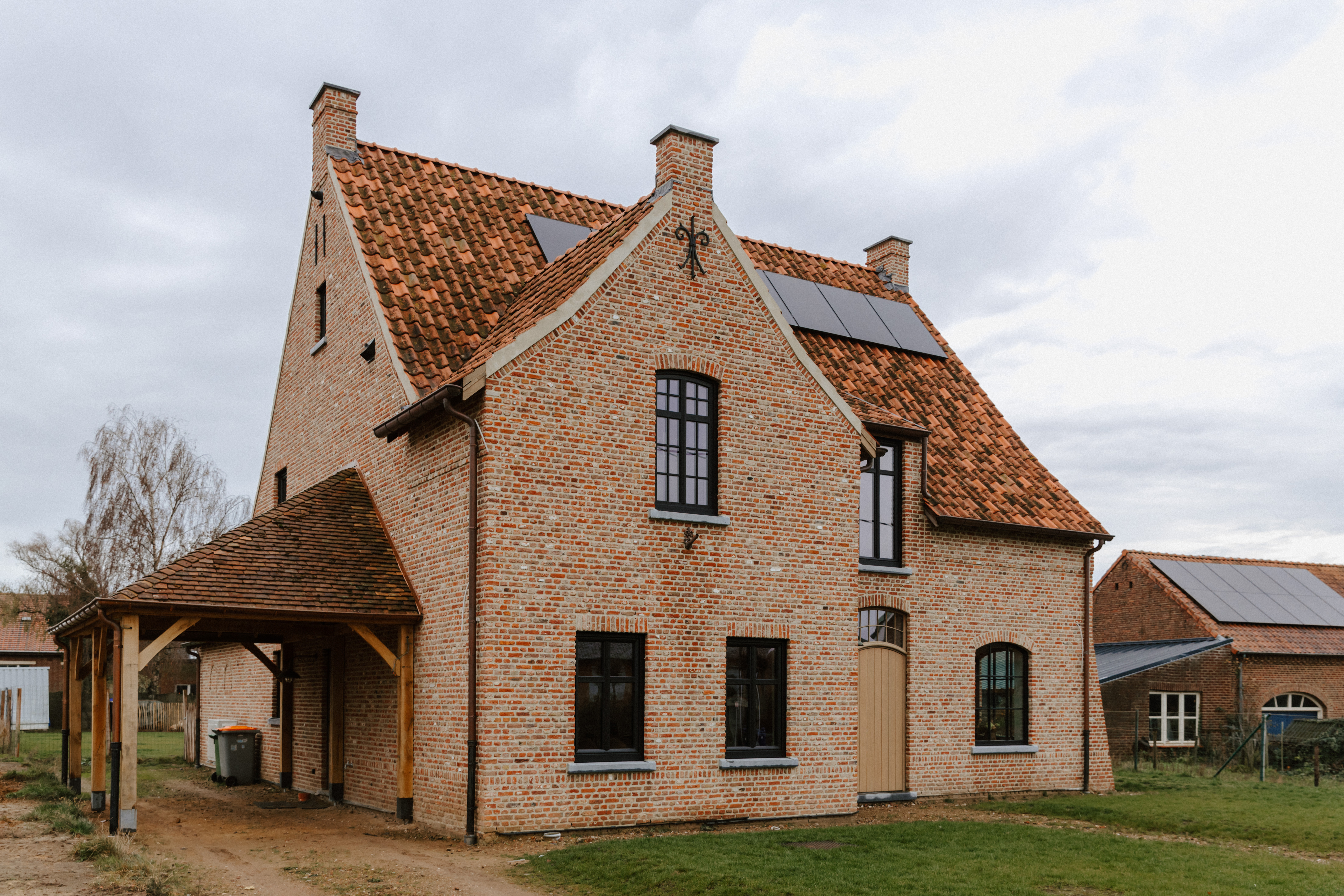 Vrijstaande landelijke bakstenen woning met donkere houten ramen, waaronder een vast raam en een draai-kipraam, onder een rood pannendak.