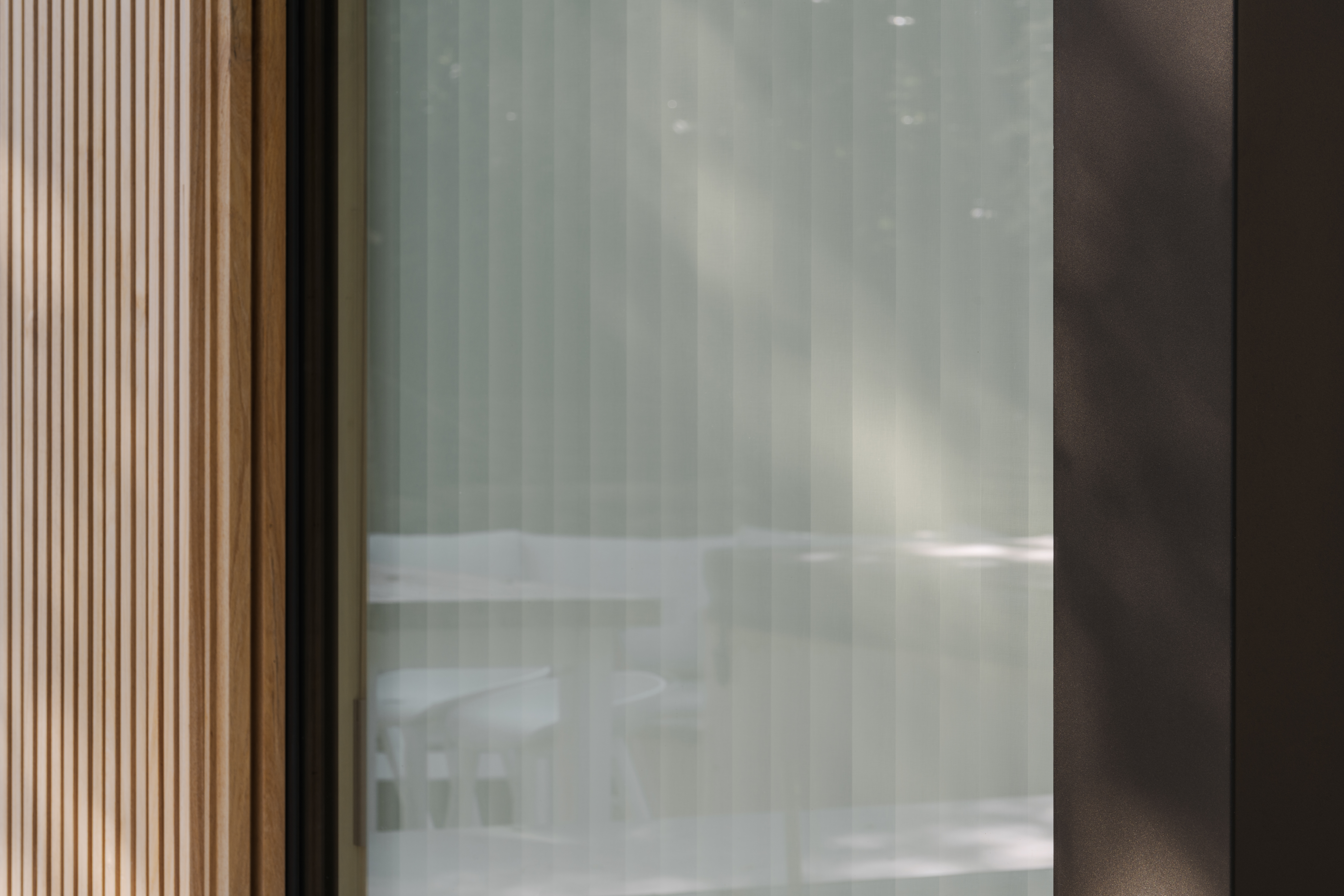 Modern Koncept-vast raam met zwarte raamprofielen, naast een verticale houten wandbekleding en een licht gordijn in een karaktervolle nieuwbouw.