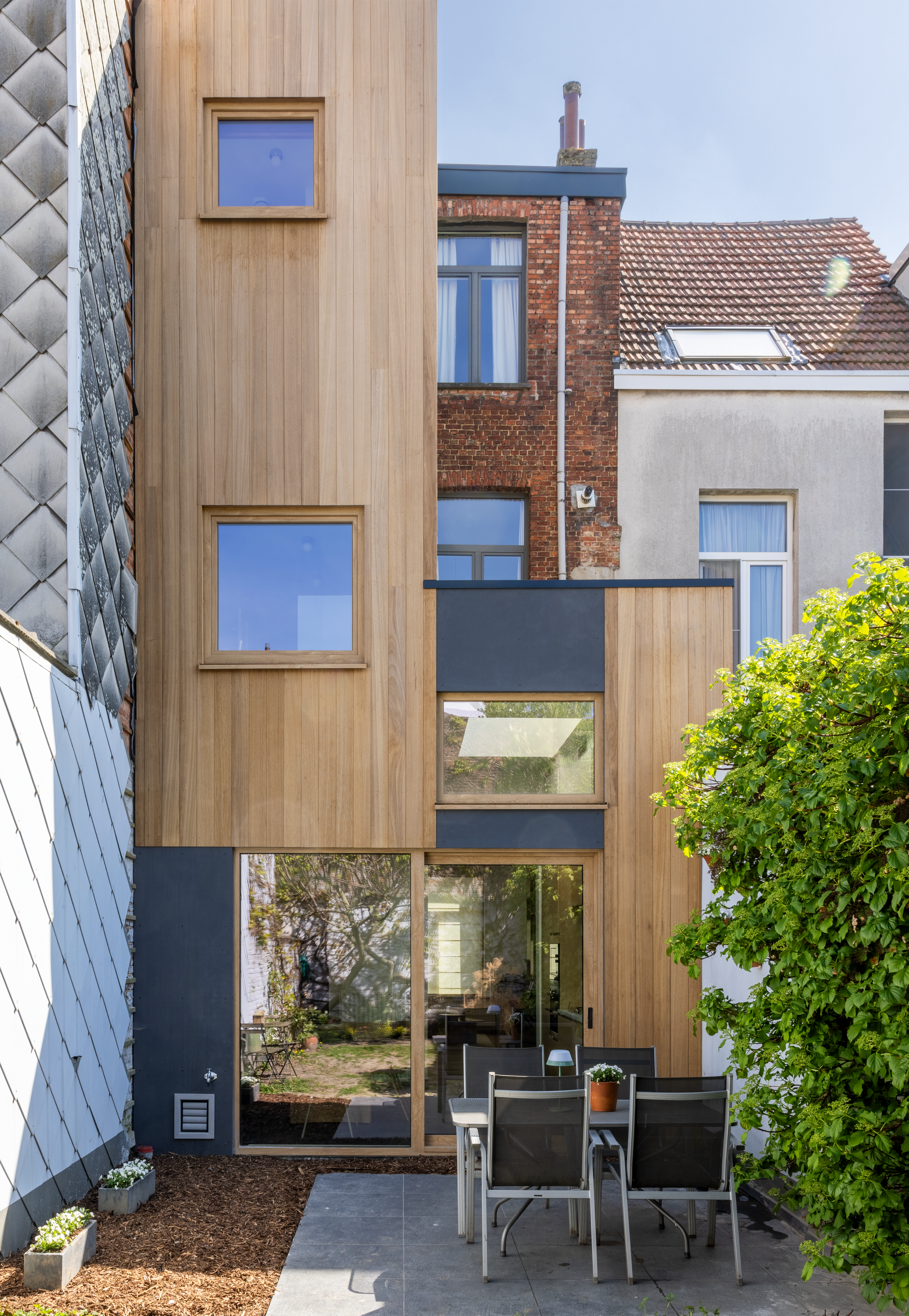 Hedendaagse rijwoning met verticale gevelbekleding in natuurlijke eiklook, vaste ramen en draai-kipramen met donkere raamprofielen.