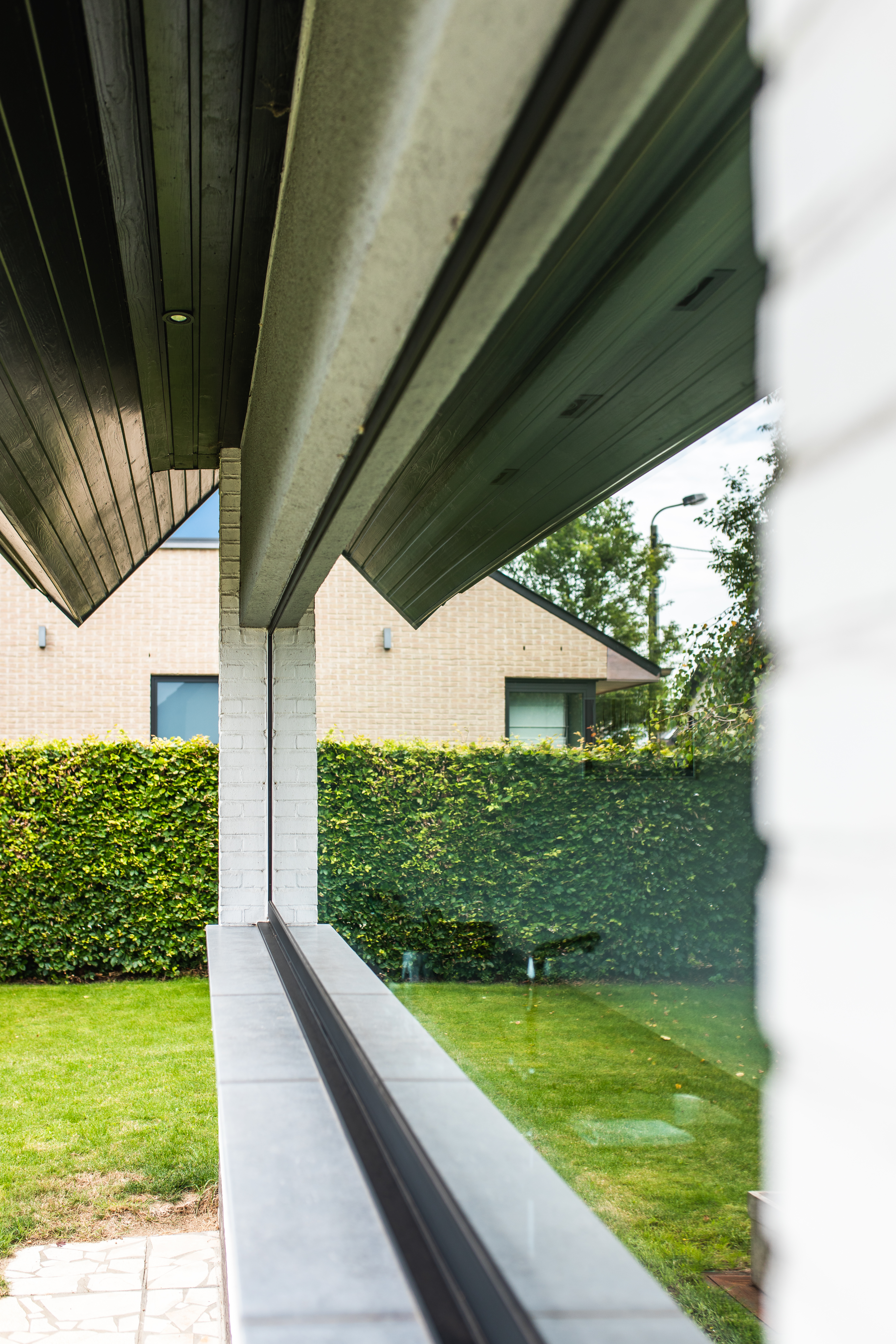 Vast raam met zwarte raamprofielen in een karaktervolle, moderne woning na renovatie, met zicht op de tuin, haag en bakstenen gevel.