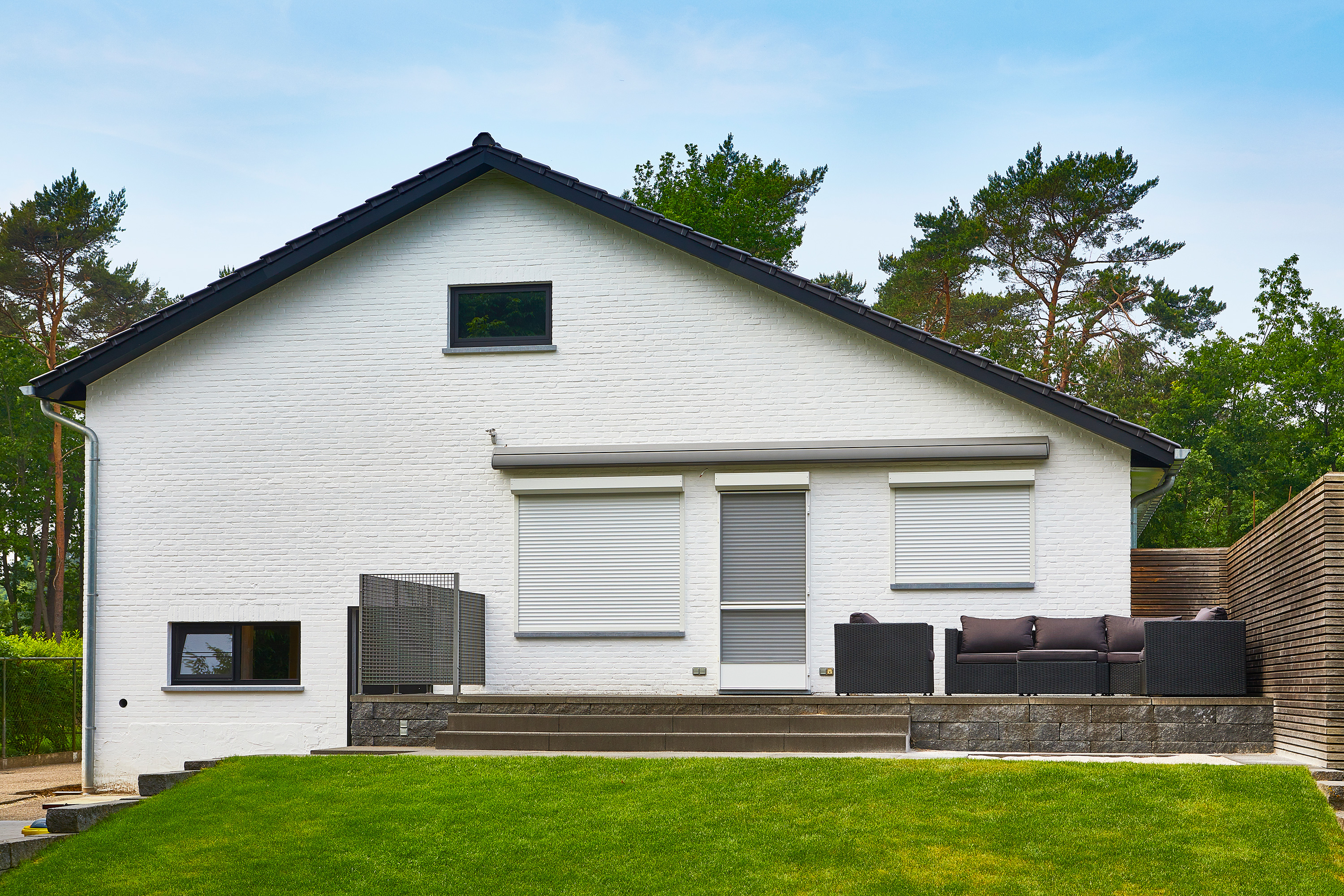 Moderne gerenoveerde vrijstaande woning met witte gevel, zwarte Steellook-ramen en zwarte voorzetrolluiken aan het terras.