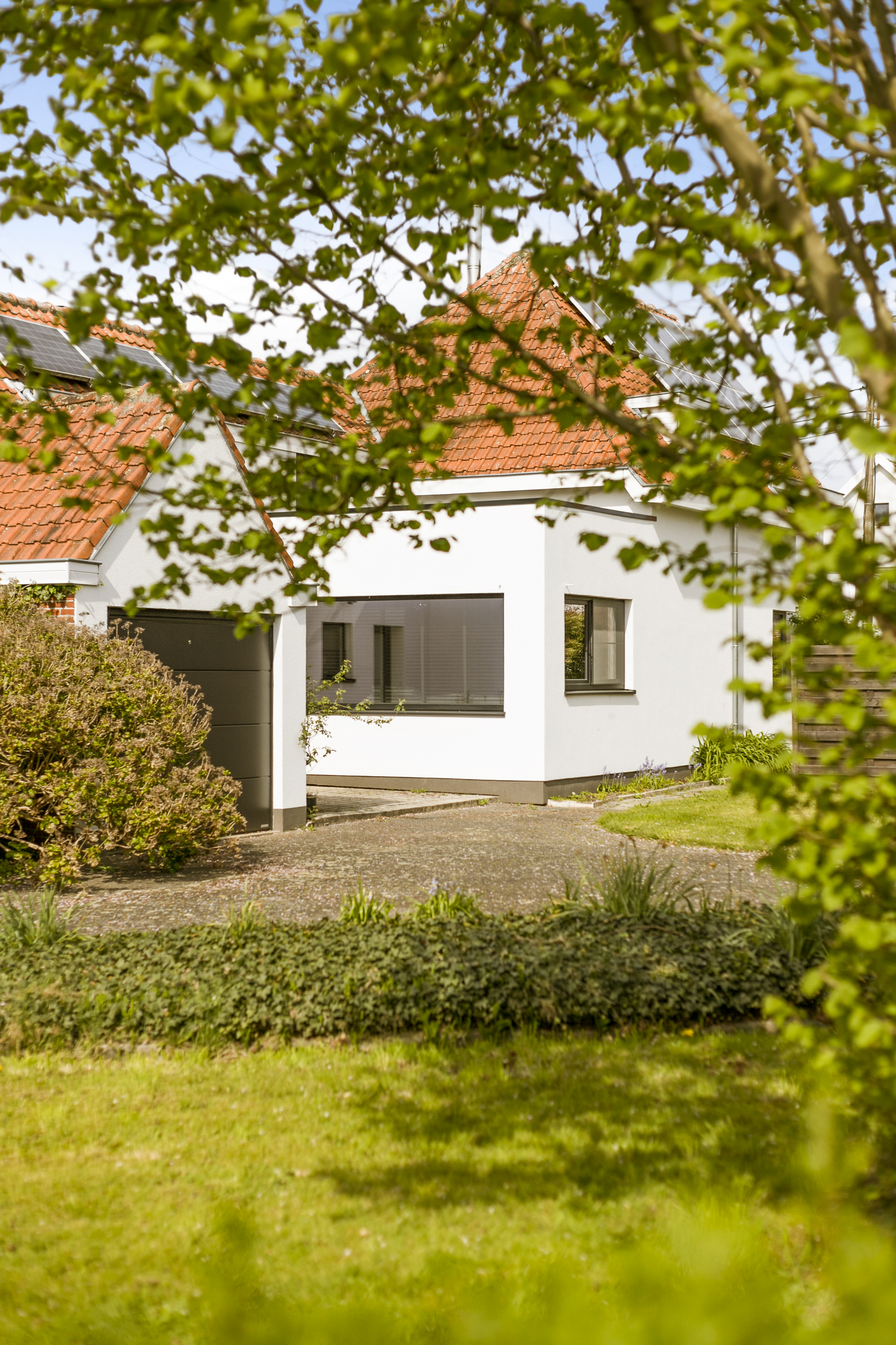 Gerenoveerde open bebouwing met witte gevel, rode pannendaken en matzwarte ramen, omgeven door een groene tuin in een gezellige, tijdloze stijl.