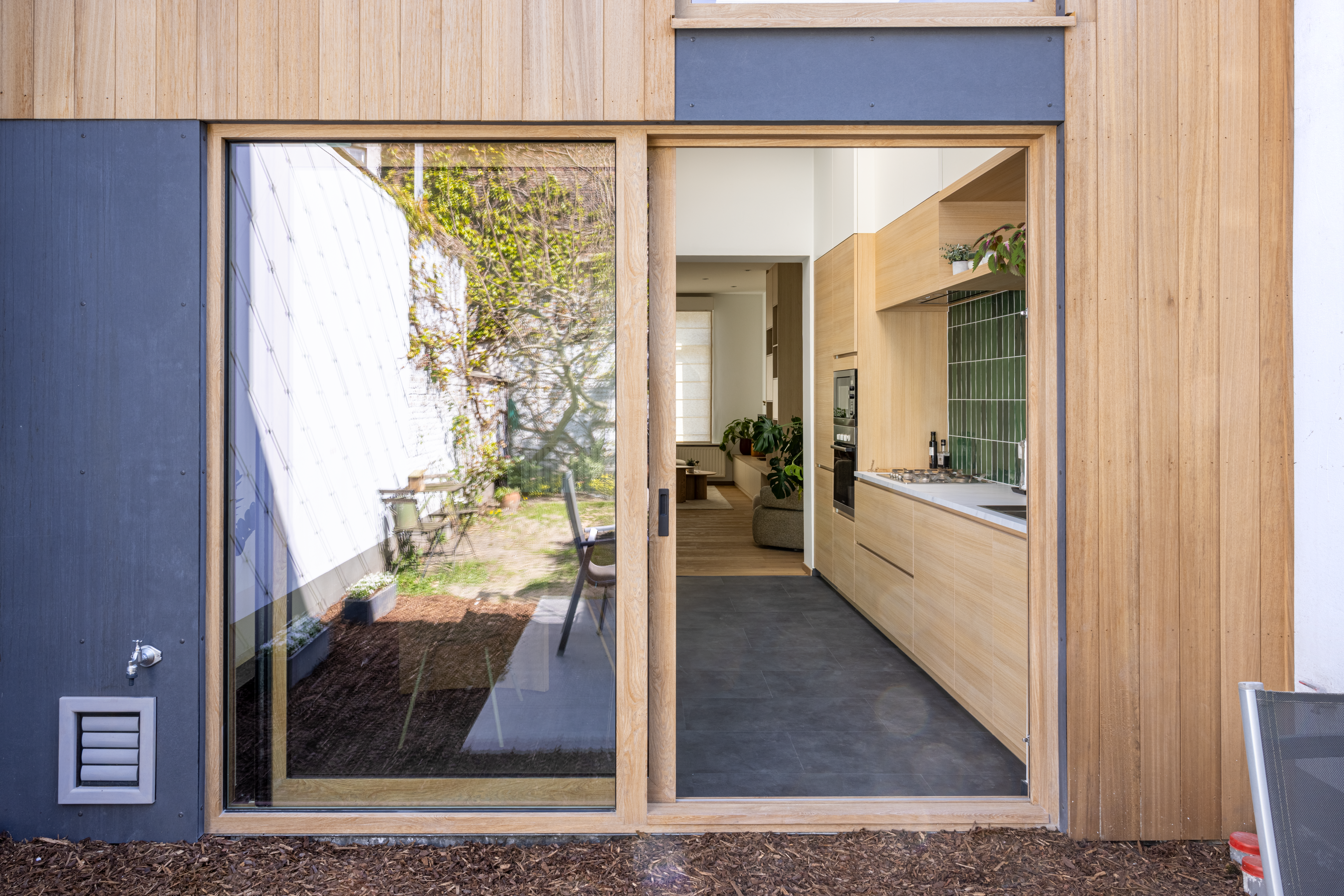 Groot ALU Visoglide Monorail-schuifraam met natuurlijke Woodec Eik Natuur Nerf-afwerking, geïntegreerd in een gerenoveerde rijwoning met zicht op de keuken.