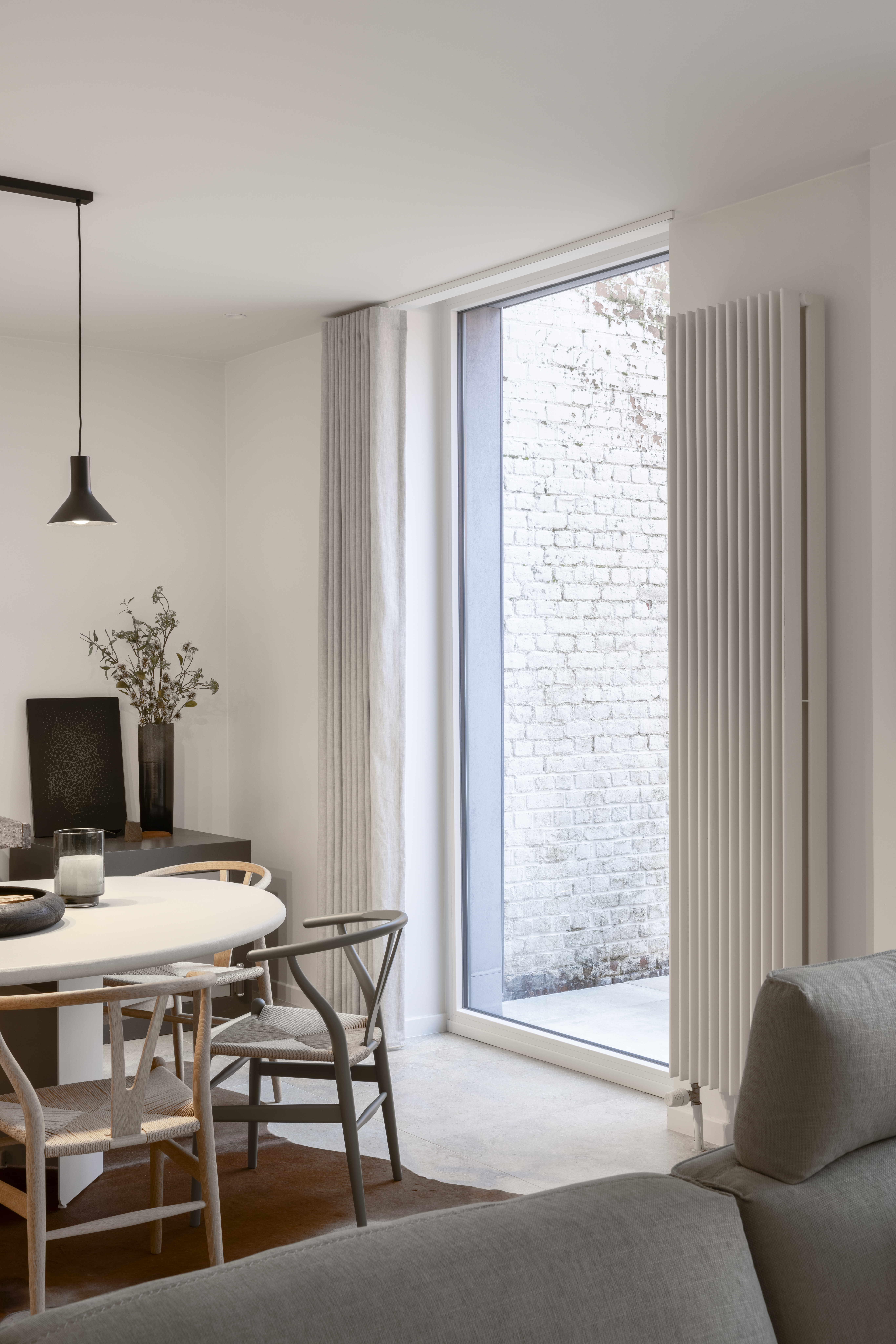 Modern gerenoveerd interieur met een vast raam met witte raamprofielen, naast een lichte bakstenen muur en een sobere radiator.