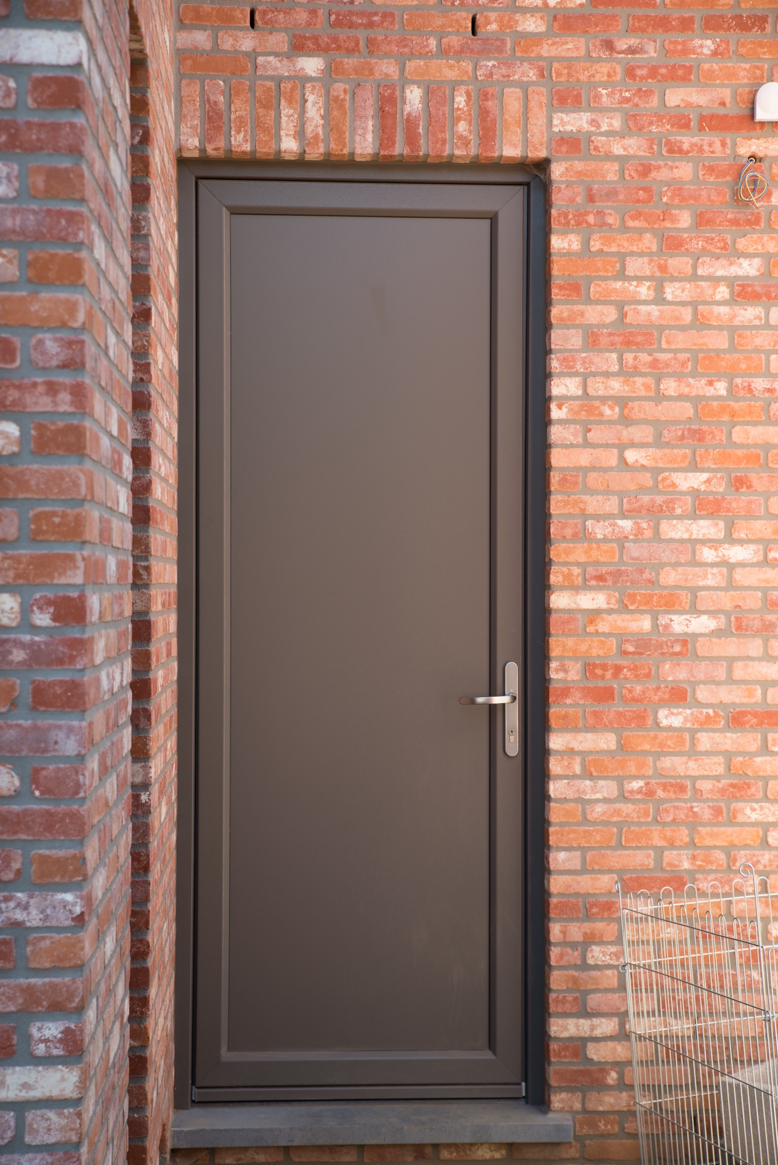 Donker kwartsgrijze paneeldeur met een sobere, tijdloze uitstraling in een rode bakstenen gevel van een nieuwbouwwoning in halfopen bebouwing.