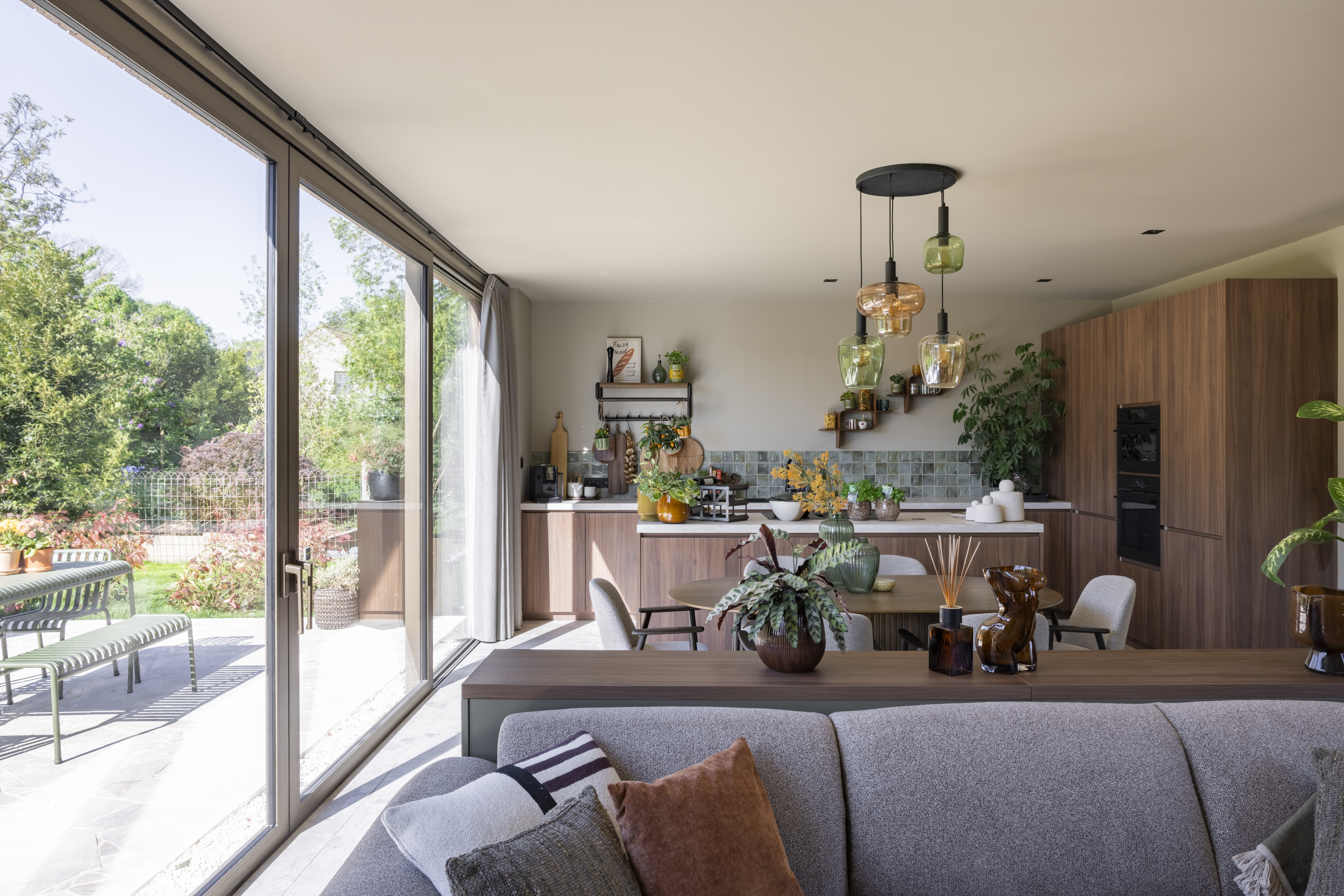 Modern interieur met een groot ALU Visoglide Monorail-schuifraam in bronsanodisatie, met zicht op het terras en de tuin.