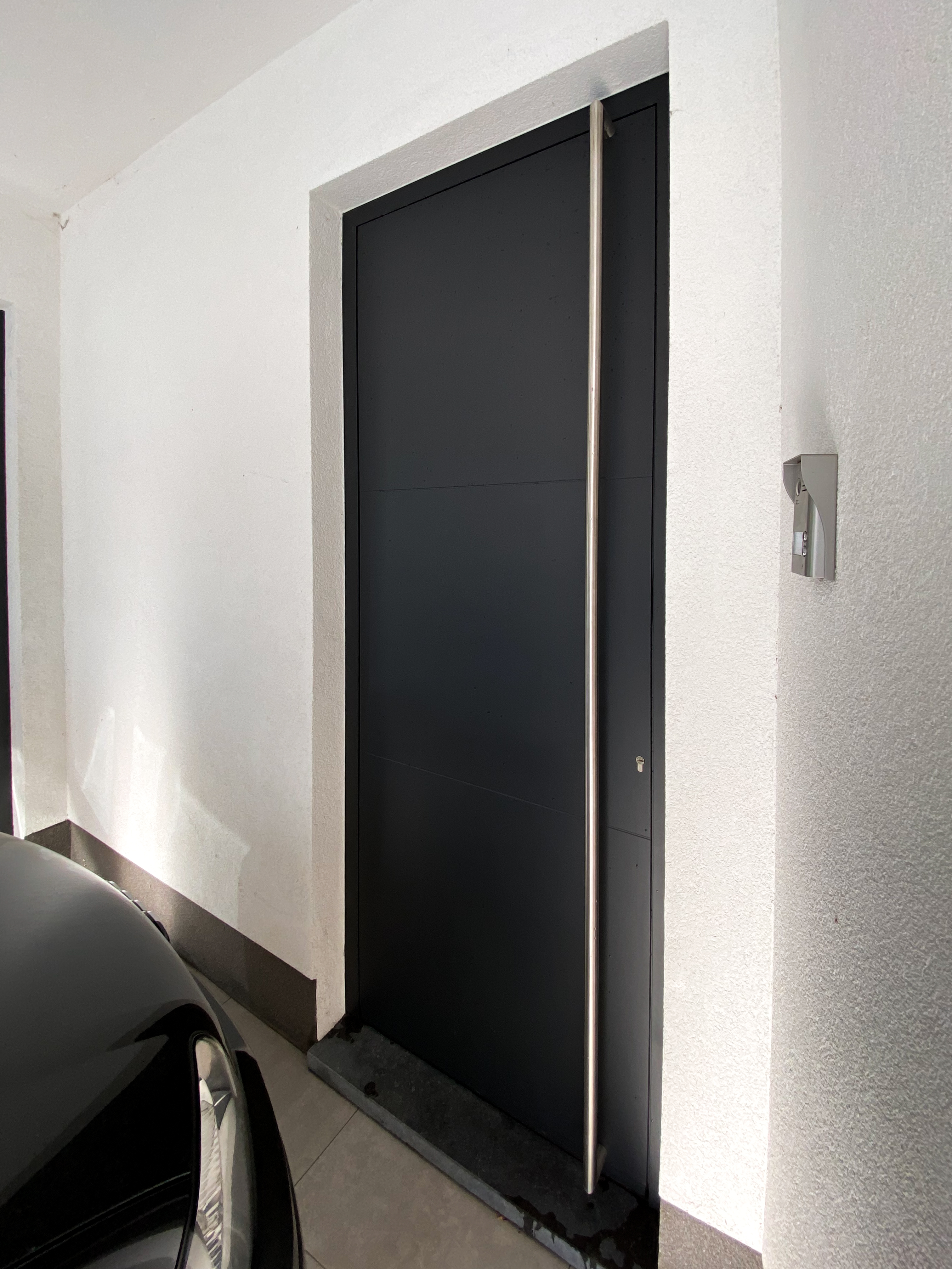 Zwart aluminium paneel van ALU Koncept in een witte wand, met een donker oppervlak en een smal kader in de inkomhal.