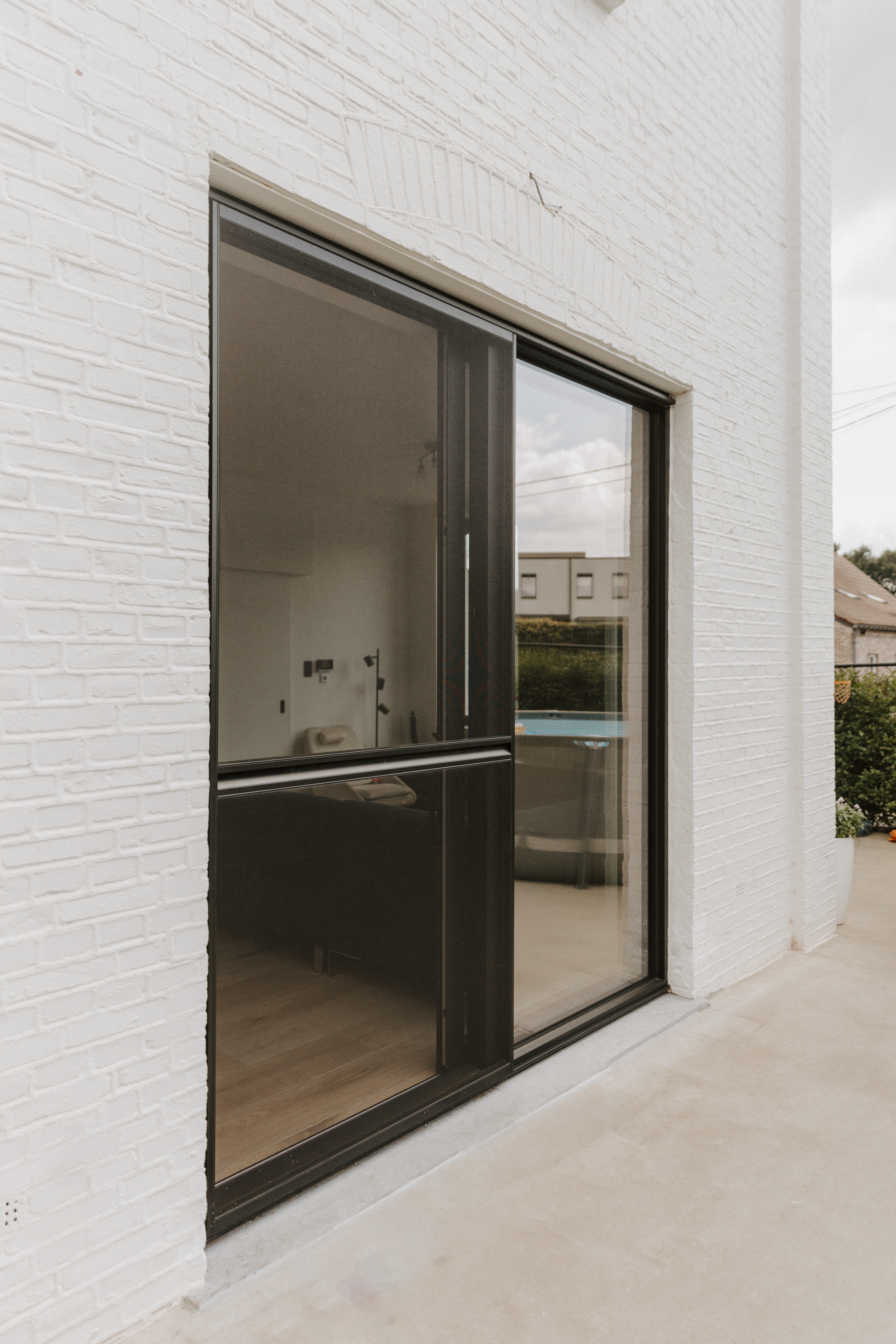 Diepzwart aluminium schuifvliegenraam in een lichte bakstenen gevel, met slanke profielen en zicht op het interieur en de omgeving.